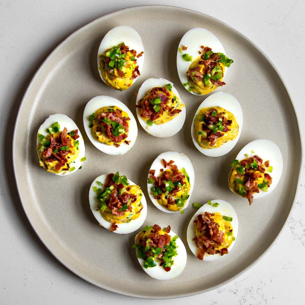 devilled eggs on a beige plate topped with bacon and jalapeno.