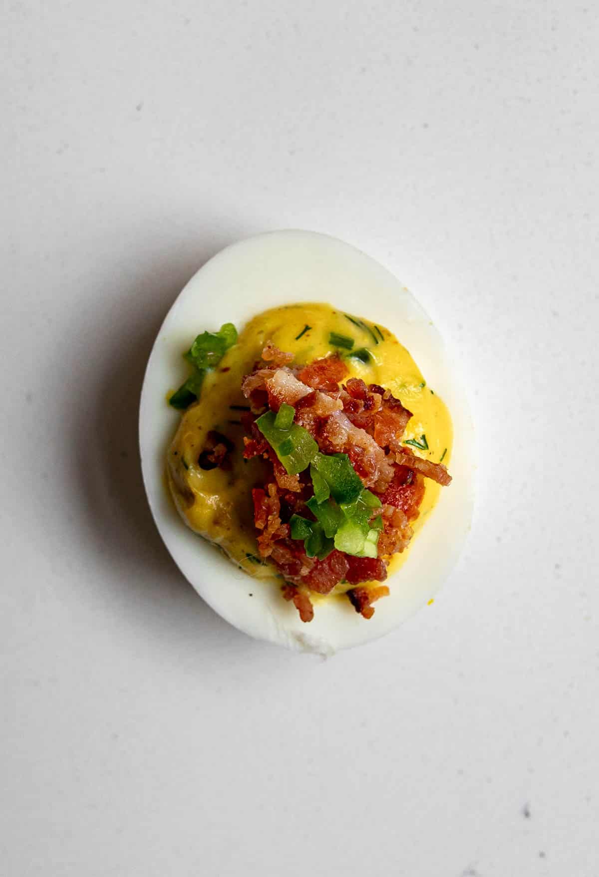 a single deviled egg topped with bacon and jalapeno on a table.