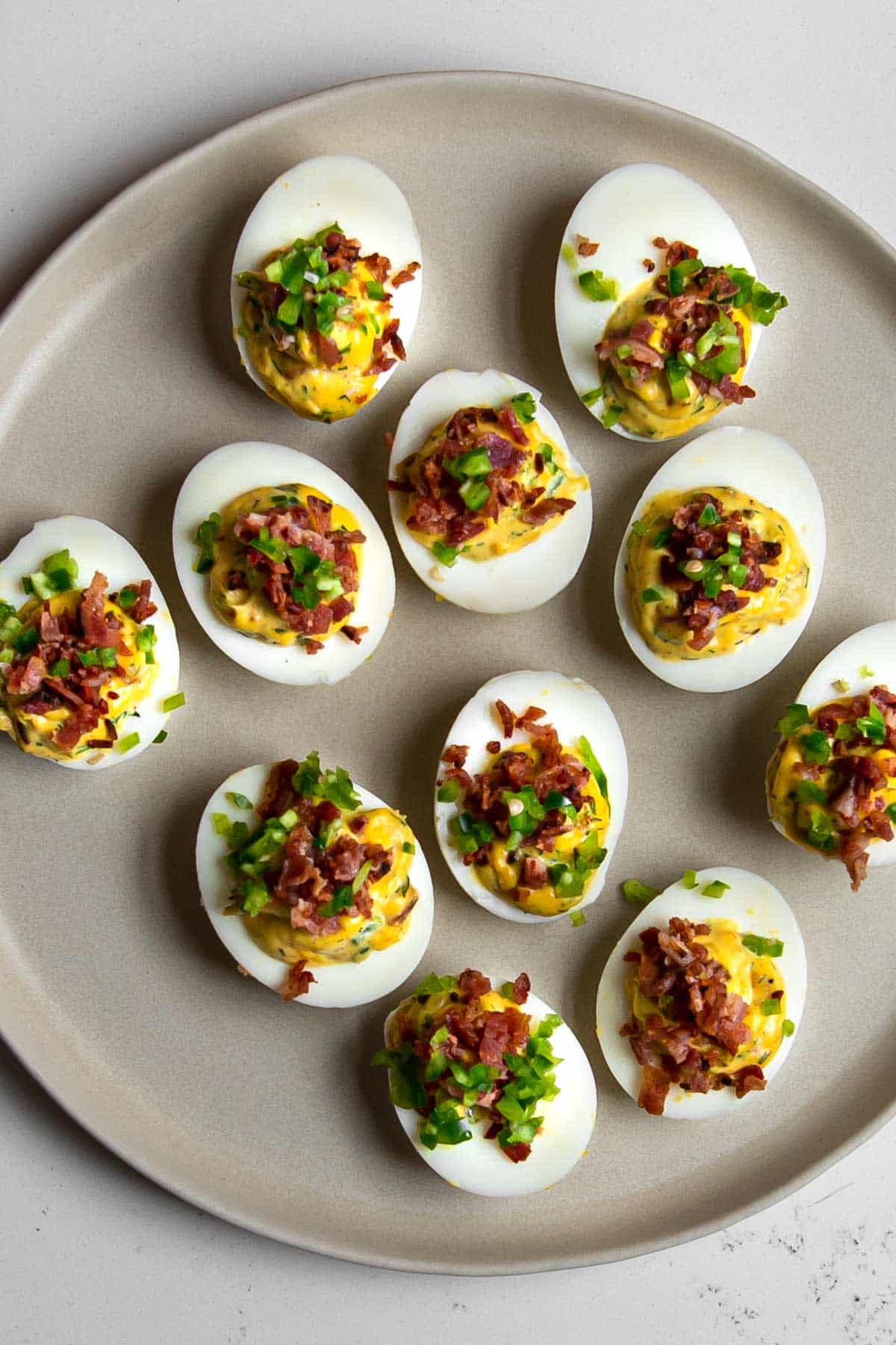devilled eggs on a beige plate topped with bacon and jalapeno.