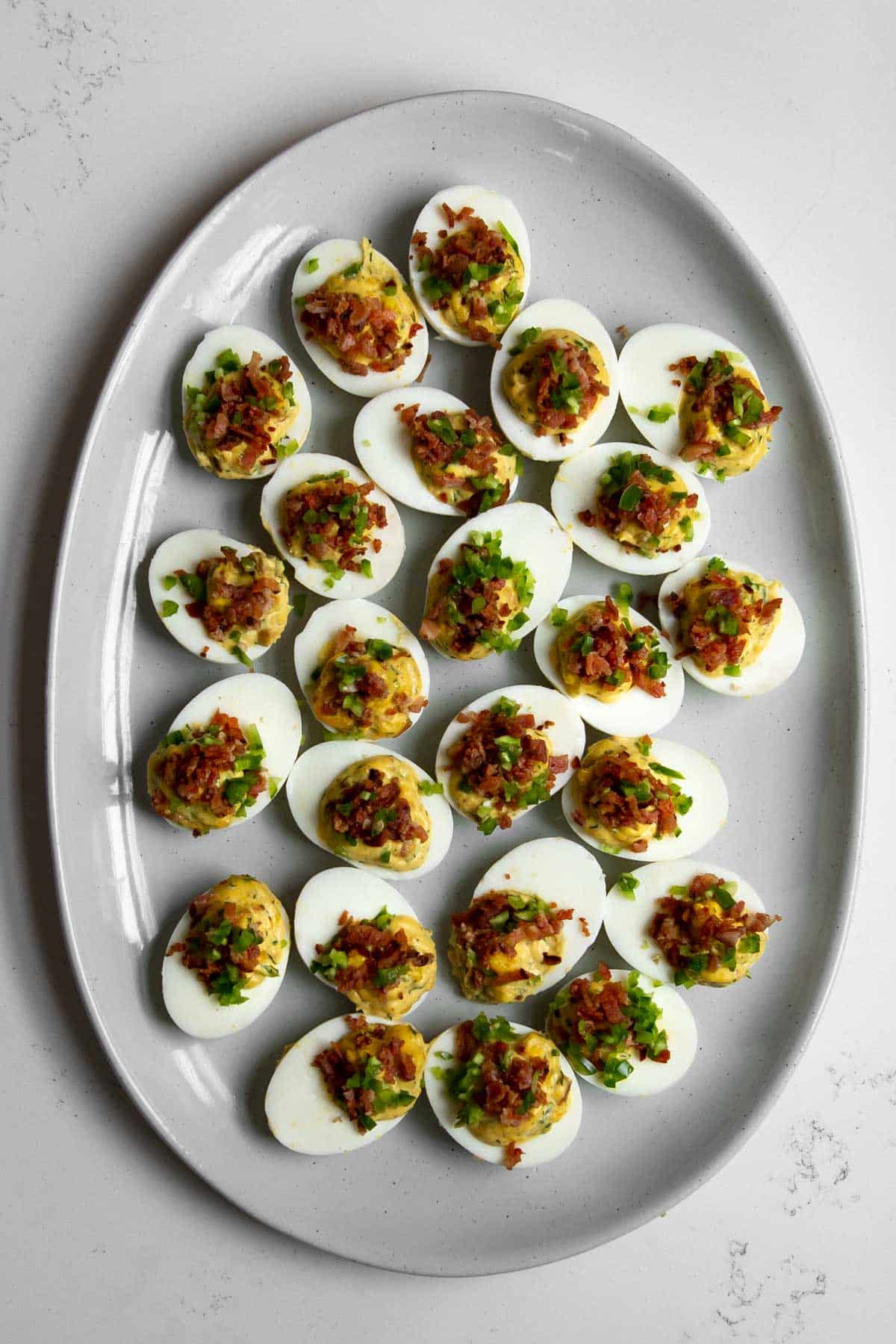 deviled eggs topped with bacon and jalapeno on a large platter.