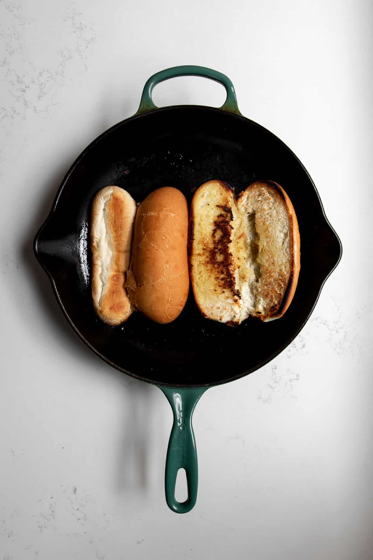 two hoagie buns toasting in a cast iron skillet.