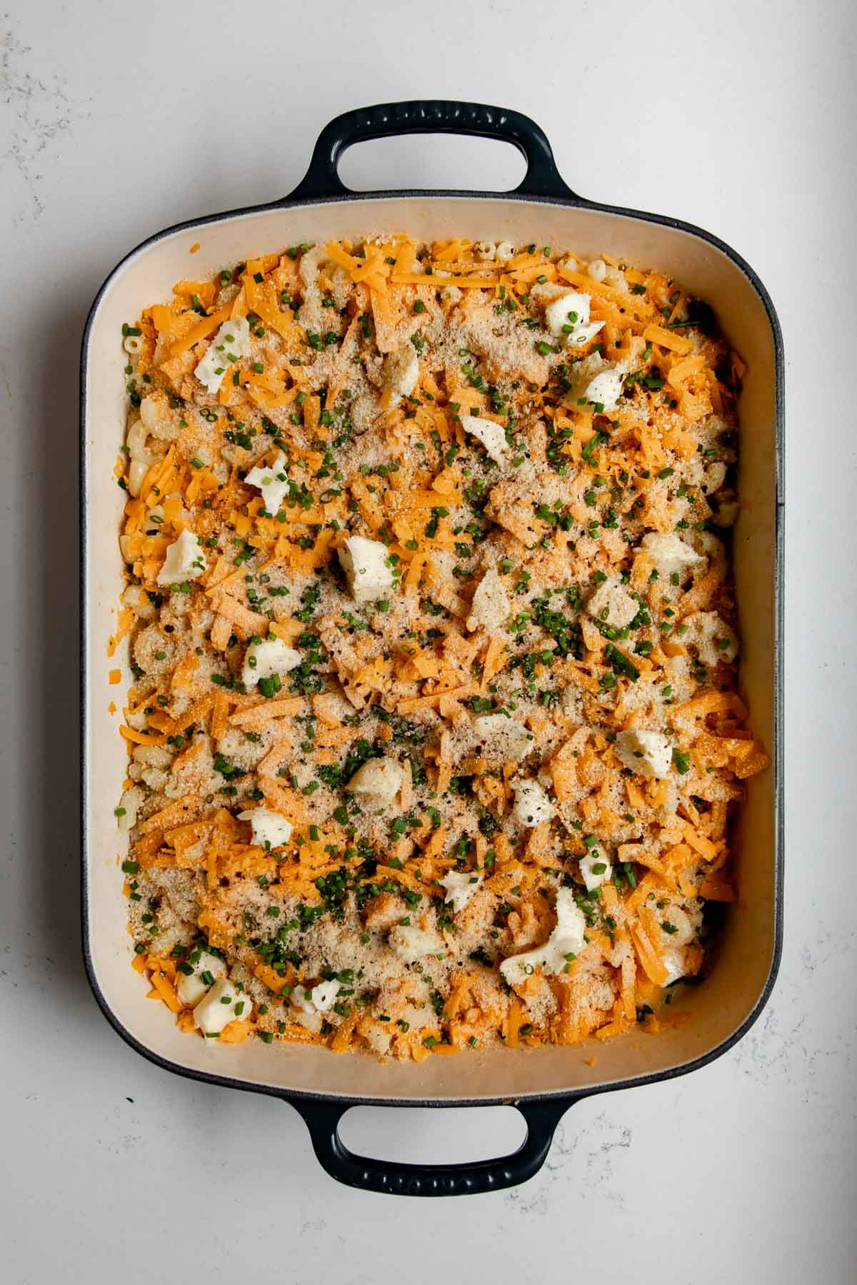 uncooked mac and cheese topped with chives and breadcrumbs in a cast-iron pan.
