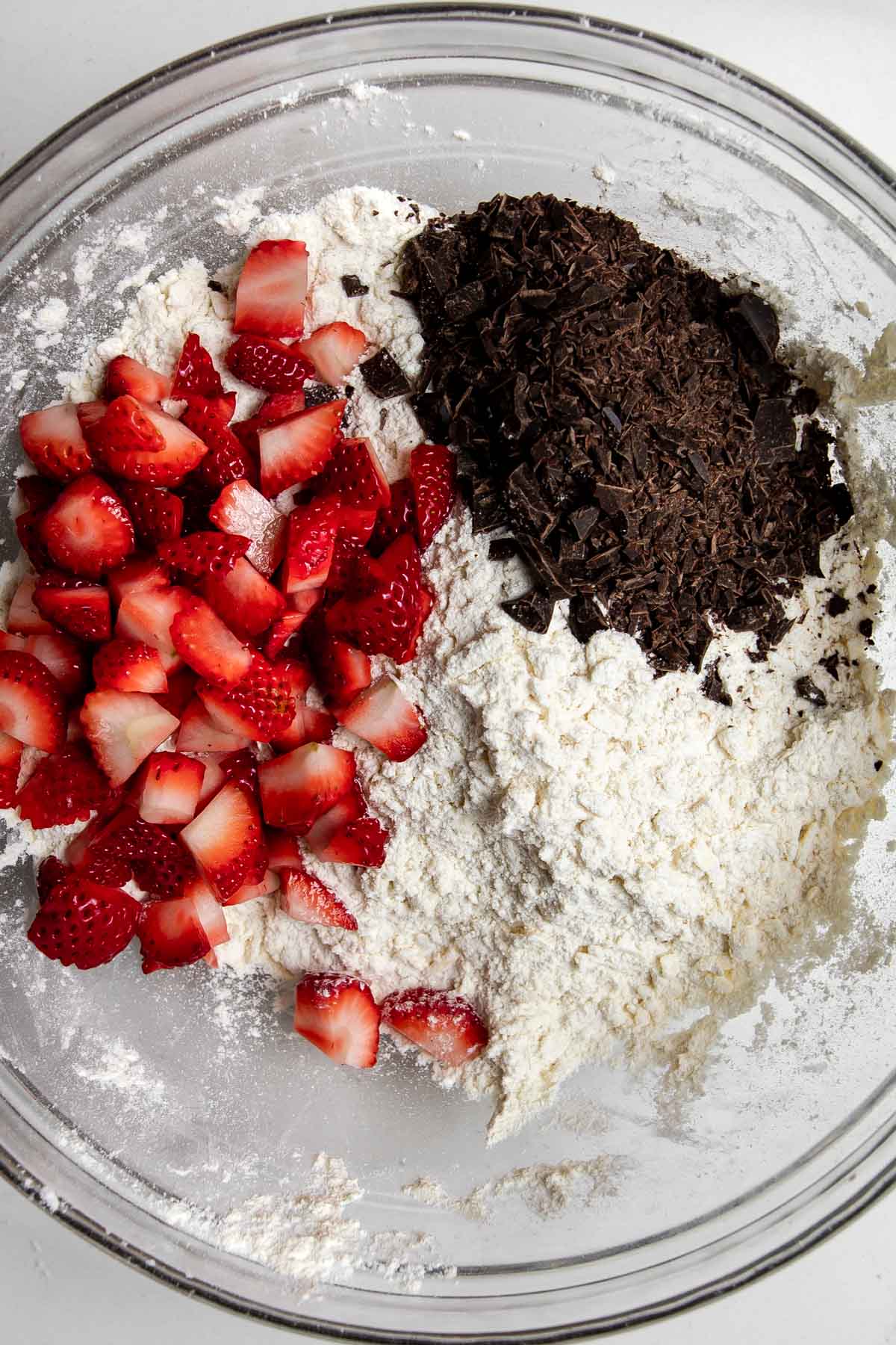 clear bowl with dry ingredients, dark chocolate and chopped strawberries.
