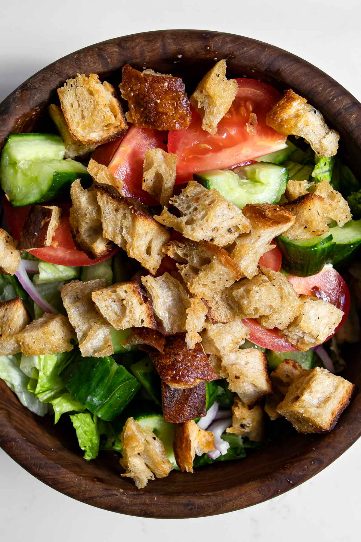 cucumber, tomato, red onions, and sourdough croutons in bowl with lettuce.