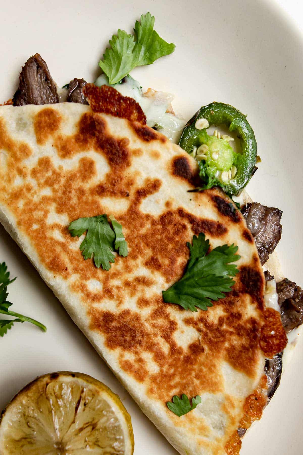 grilled carne asada quesadilla on a plate topped with cilantro.