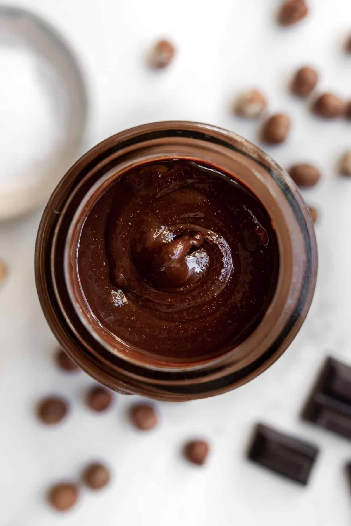 chocolate hazelnut spread in a jar with salt, chocolate squares and hazelnuts around it.