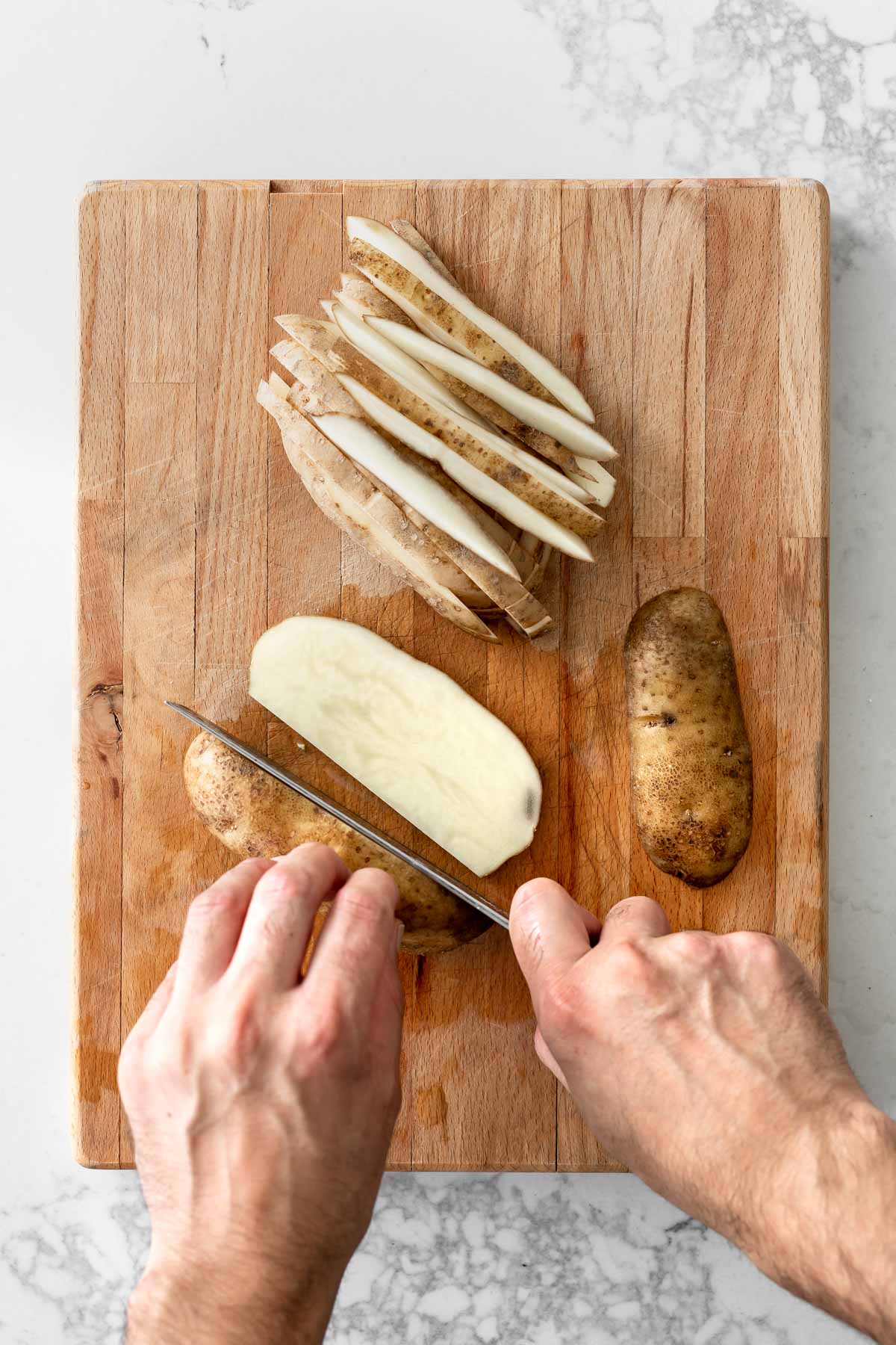 Hand cutting potatoes into fries on a cutting board.