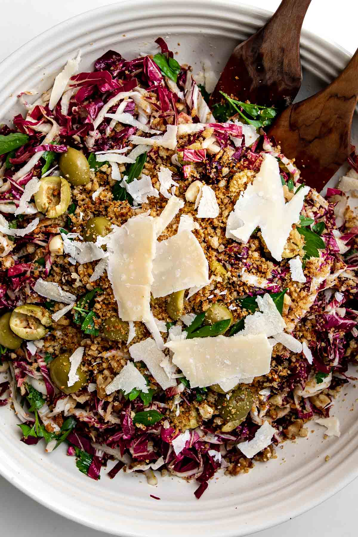 Shredded radicchio topped with pitted olives, bread crumbs, parmesan and parsley in a large serving bowl.