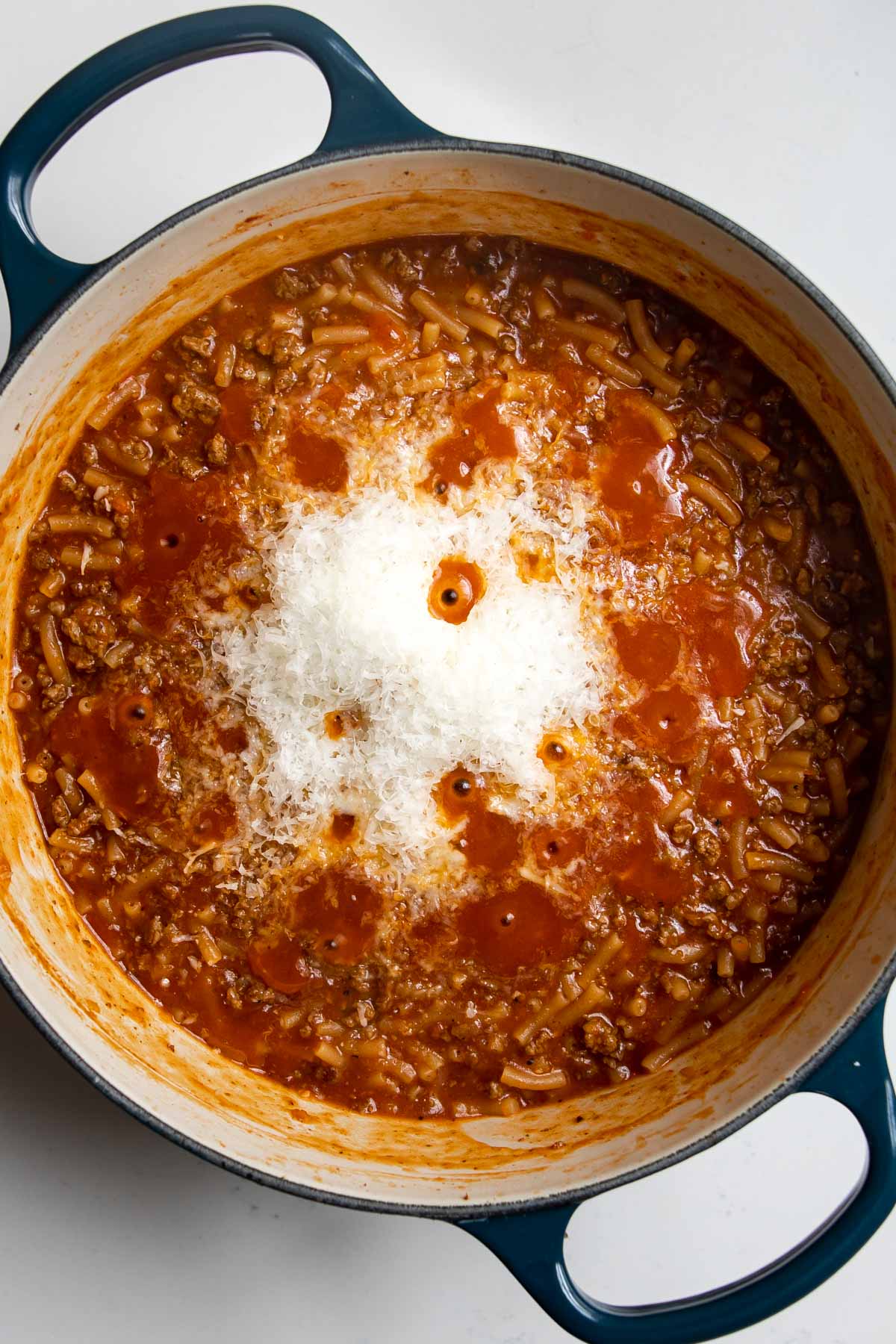 grated romano cheese on top of beefaroni in a pot.