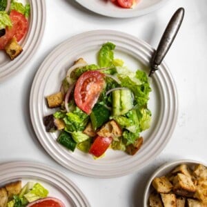 House salad topped with tomato, cucumber, sourdough croutons, and red onions on a plate with a fork.