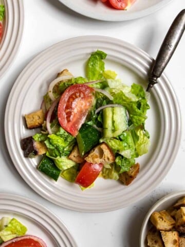 House salad topped with tomato, cucumber, sourdough croutons, and red onions on a plate with a fork.