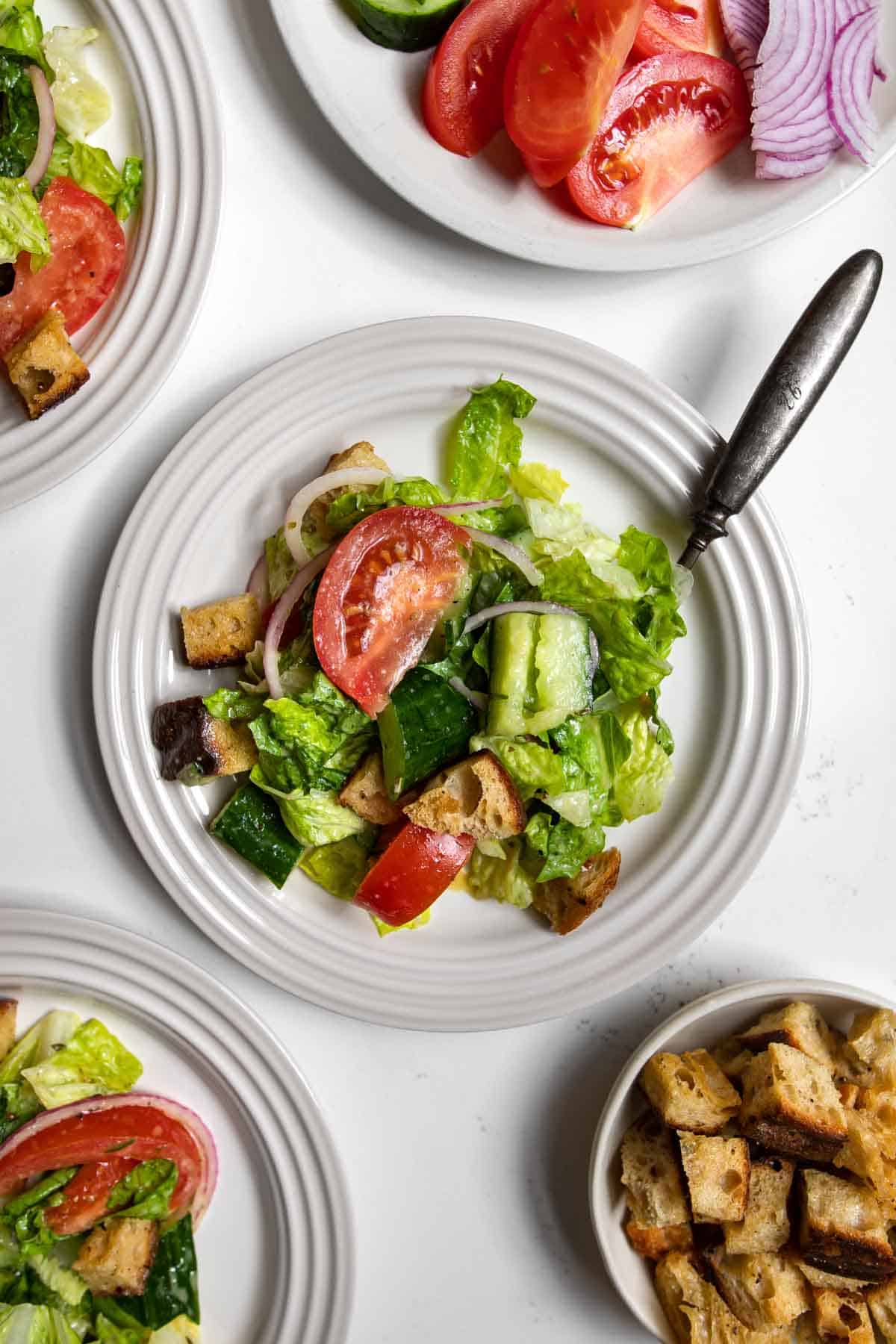 House salad topped with tomato, cucumber, sourdough croutons, and red onions on a plate with a fork.