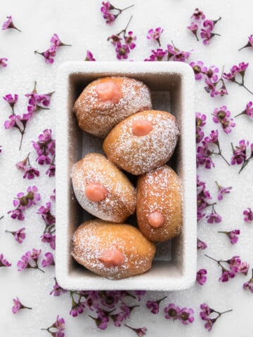 five jelly donuts in a baking dish with flowers around it.