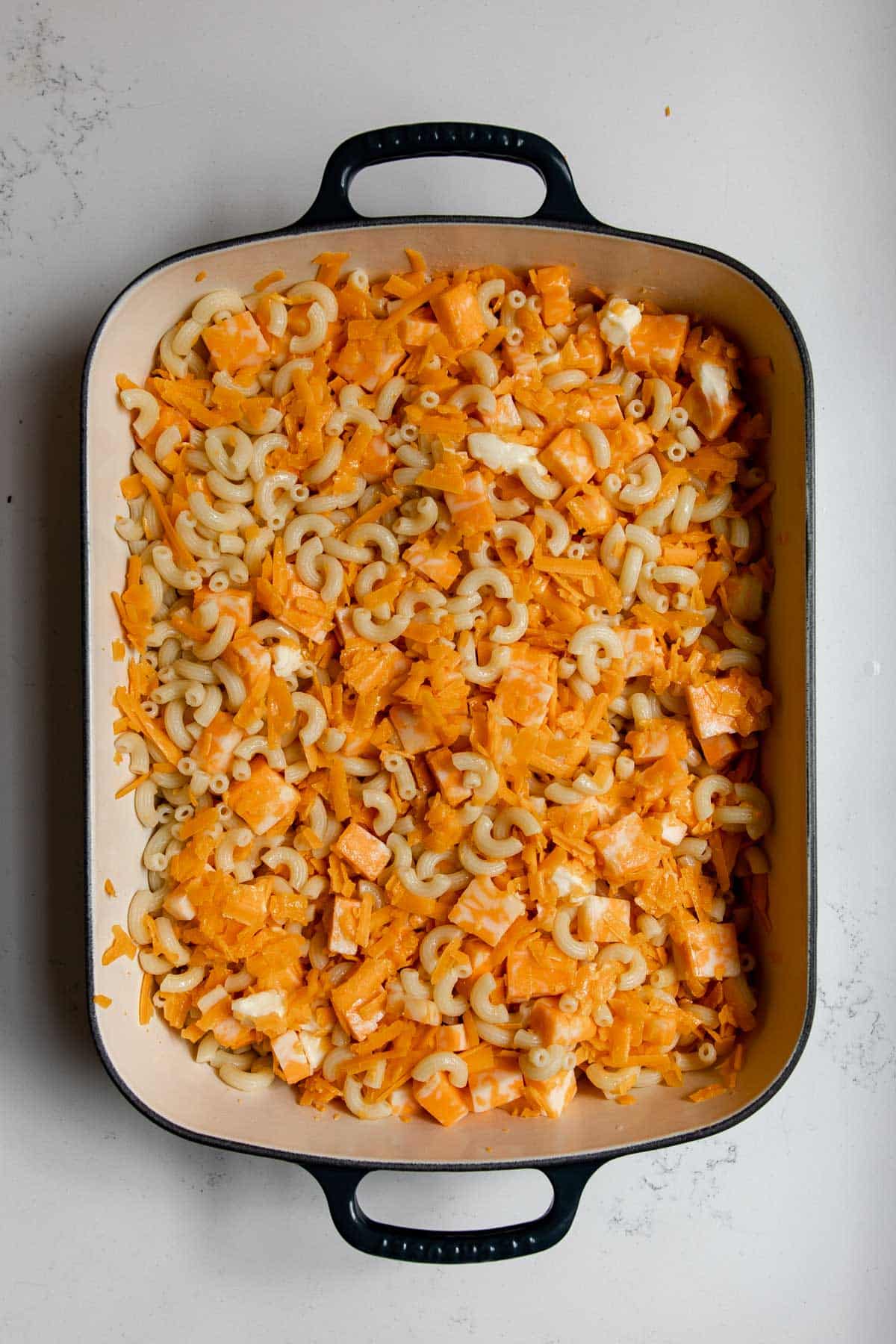 macaroni noodles tossed with cheddar cheese chunks in a cast-iron pan.