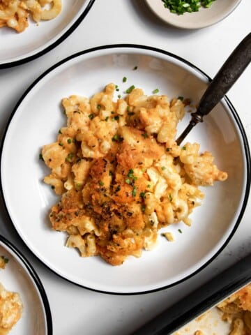 old fashioned baked macaroni and cheese in a bowl with a fork with chives on top.