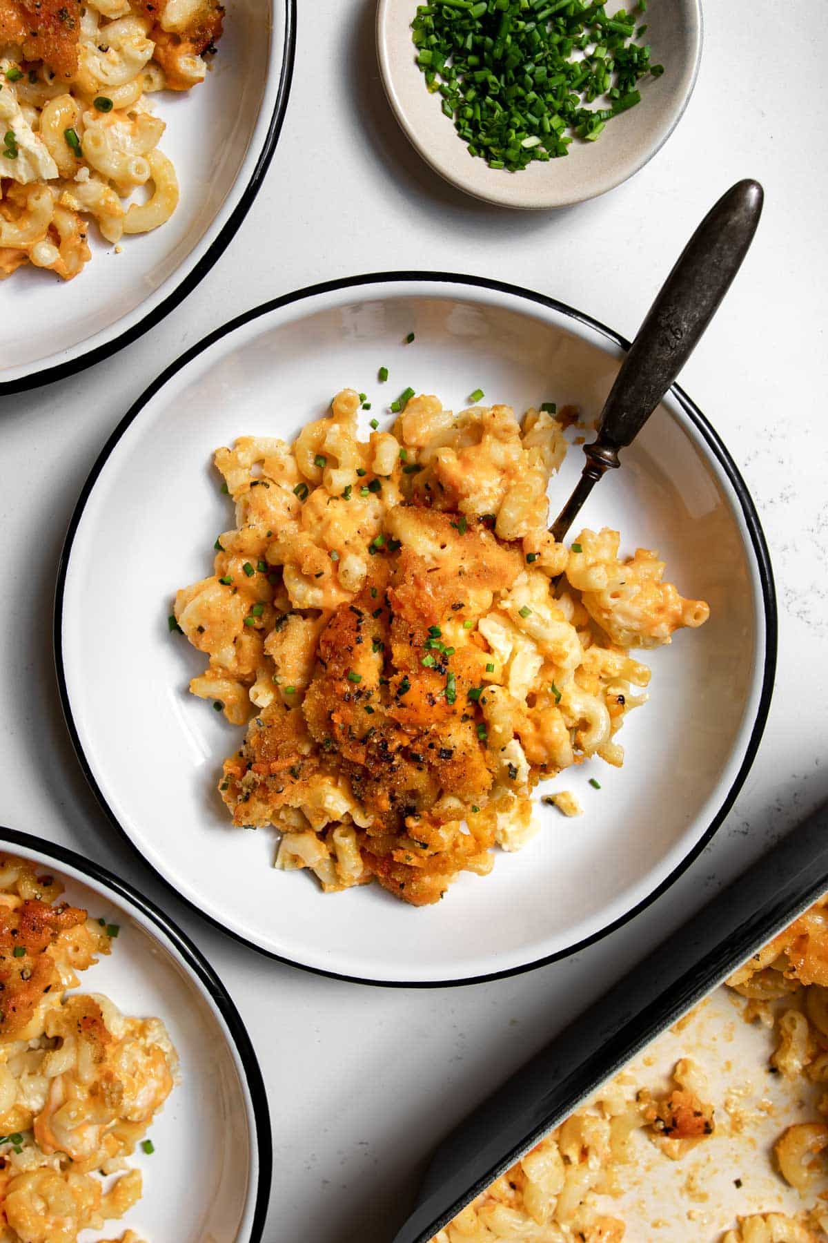 old fashioned baked macaroni and cheese in a bowl with a fork with chives on top.