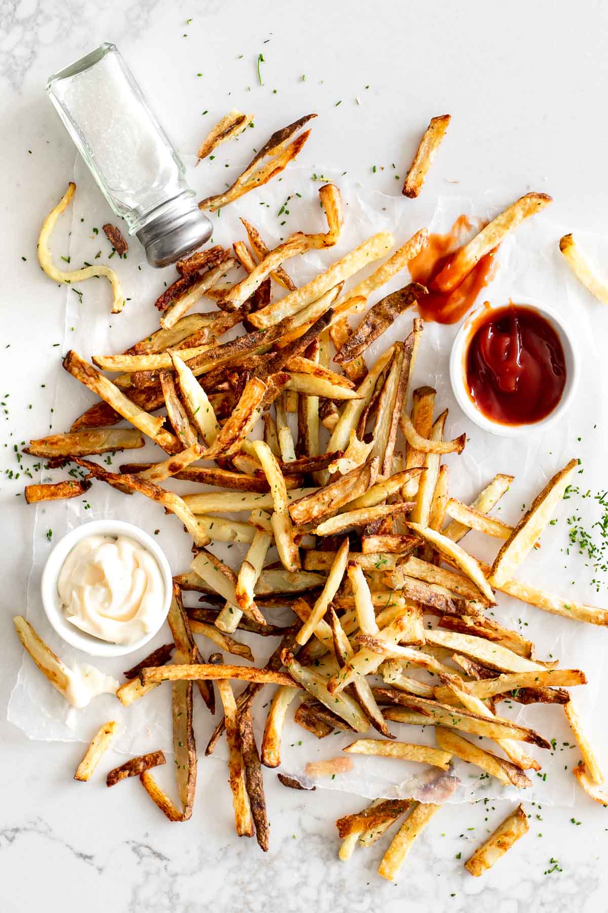 french fries on parchment paper with salt, ketchup and mayonnaise.