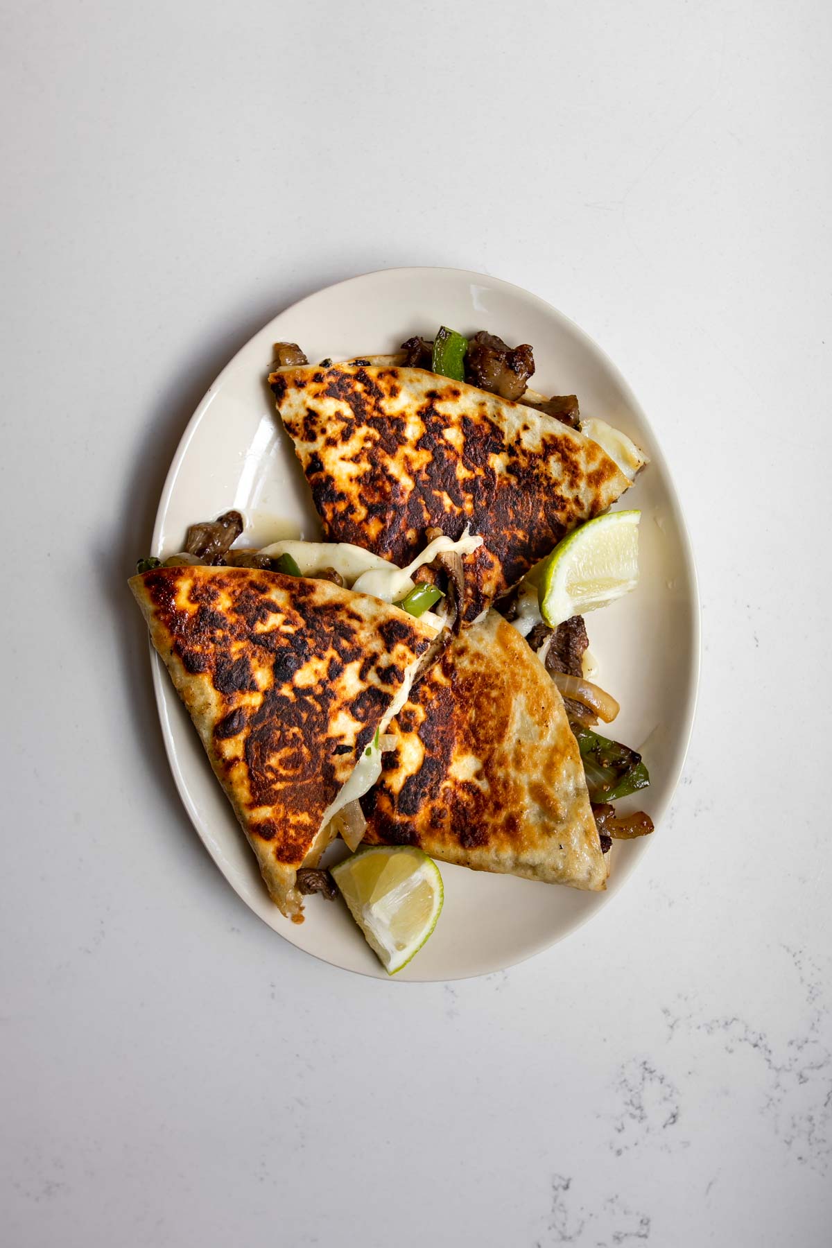 Three Philly Cheesesteak Quesadillas cut and arranged on a plate with lime wedges.