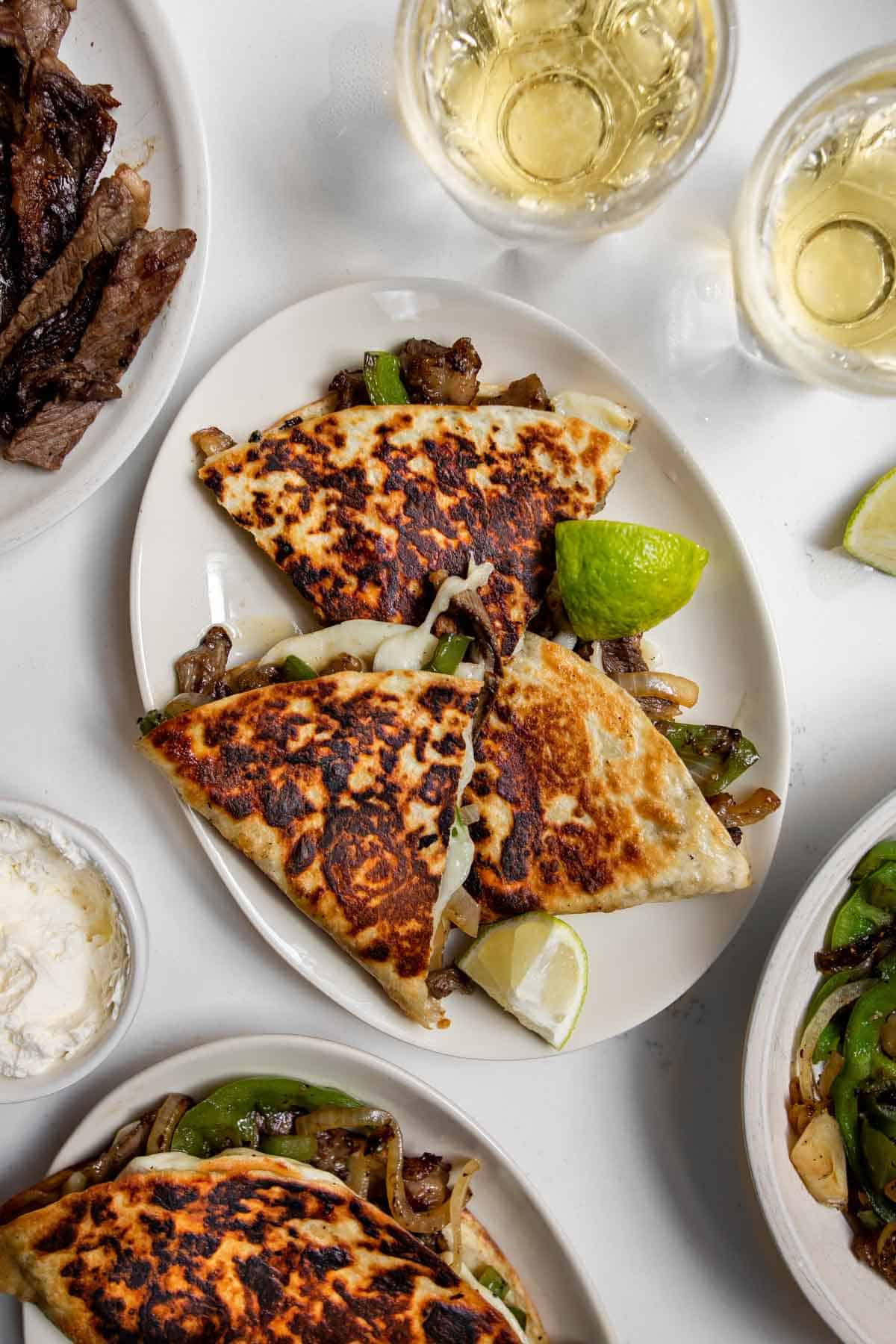 Three Philly Cheesesteak Quesadillas cut and arranged on a plate with lime wedges, beer and ingredients.