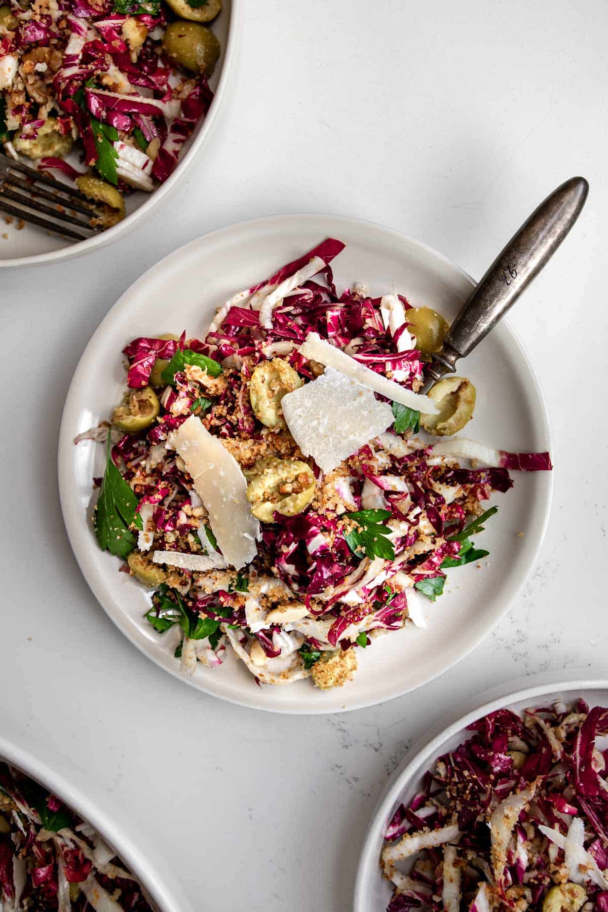 radicchio salad topped with parmesan, lemon dressing and olives on a plate with a fork.