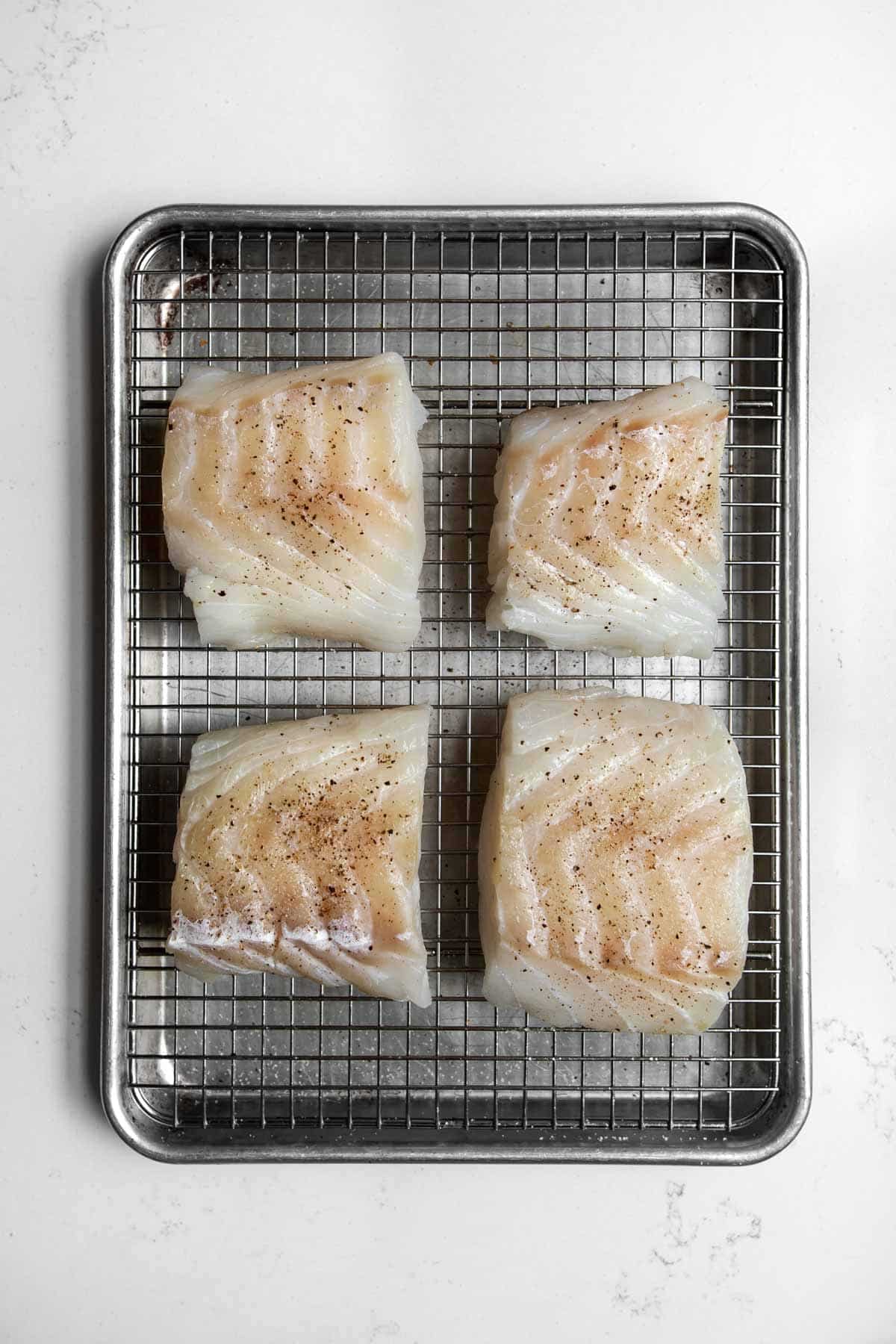 Four pieces of cod seasoned on a wire rack.