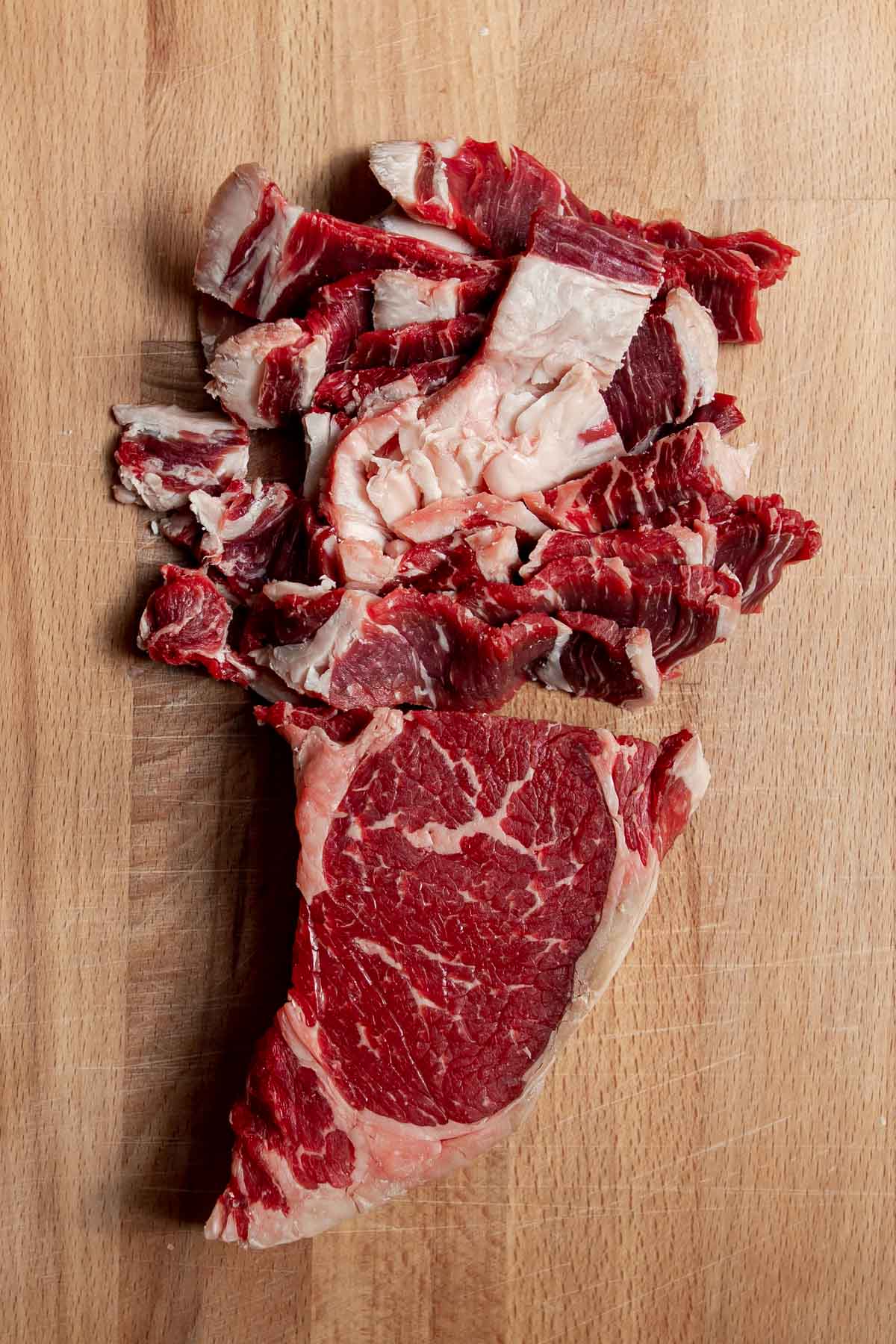 Raw ribeye steak thinly sliced on a cutting board.