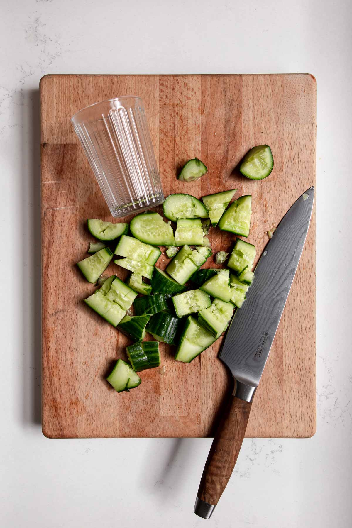 Smashed cucumbers on a cutting board with a knife and glass.