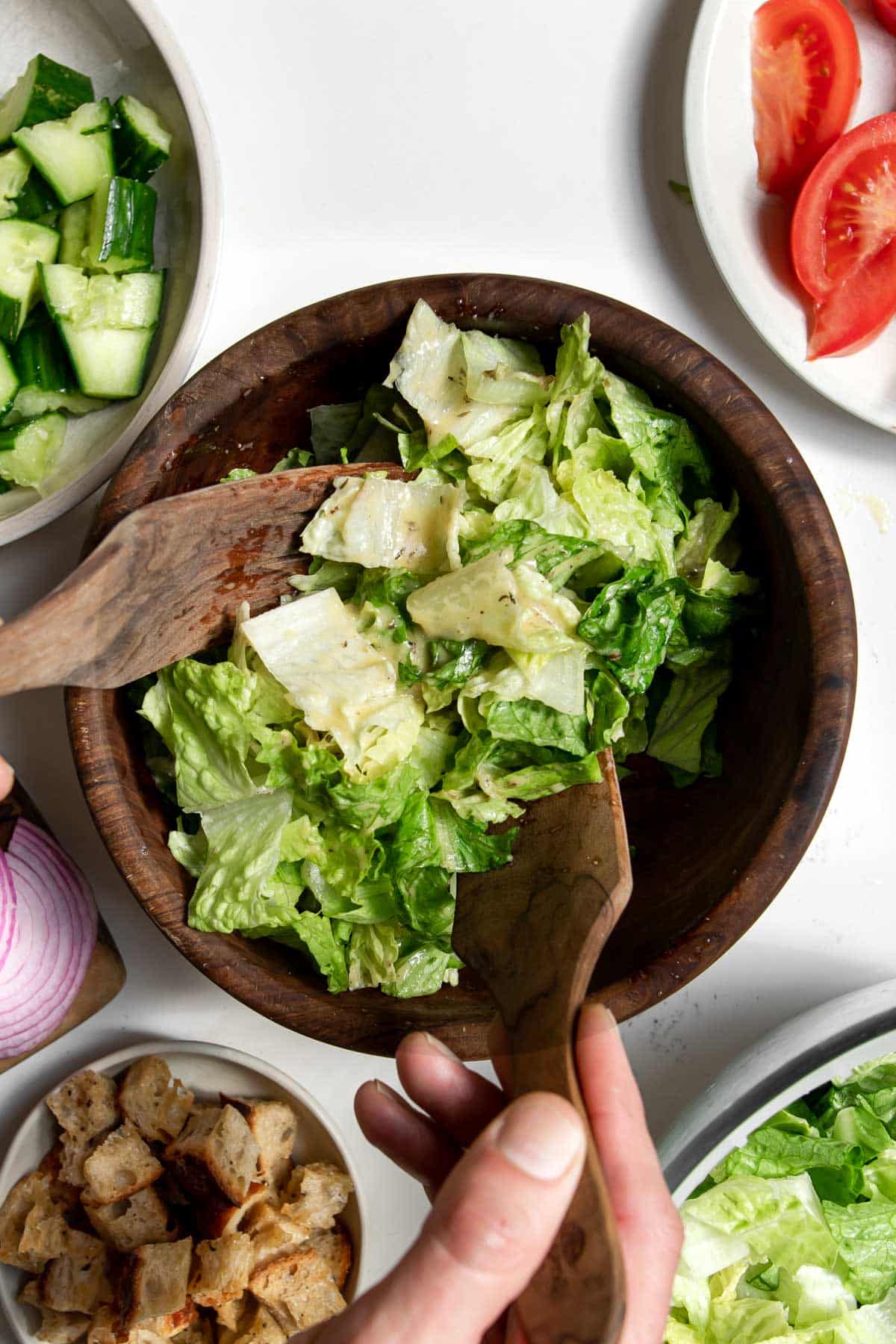 Hands tossing romaine lettuce with honey Dijon vinaigrette with ingredients around it.