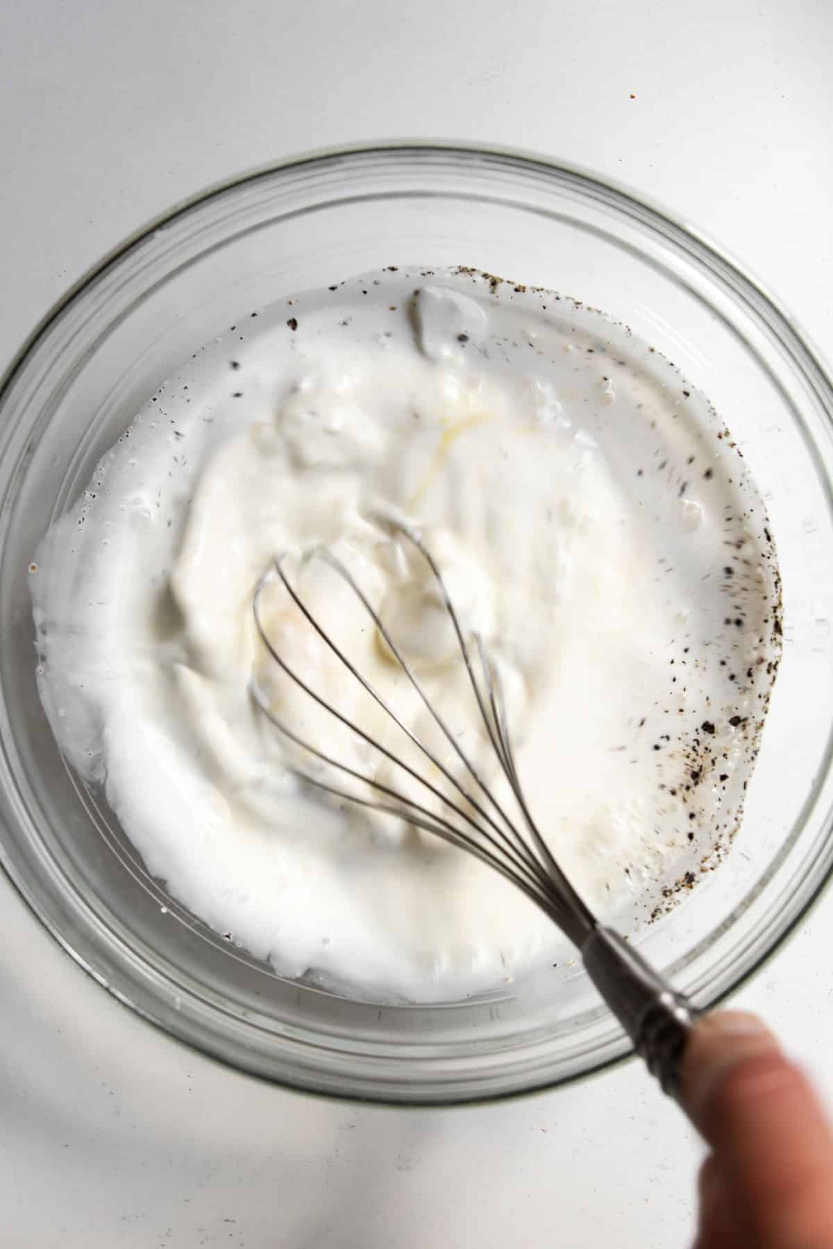 Egg, sour cream, half and half seasoned with salt and pepper in a bowl while being whisked.