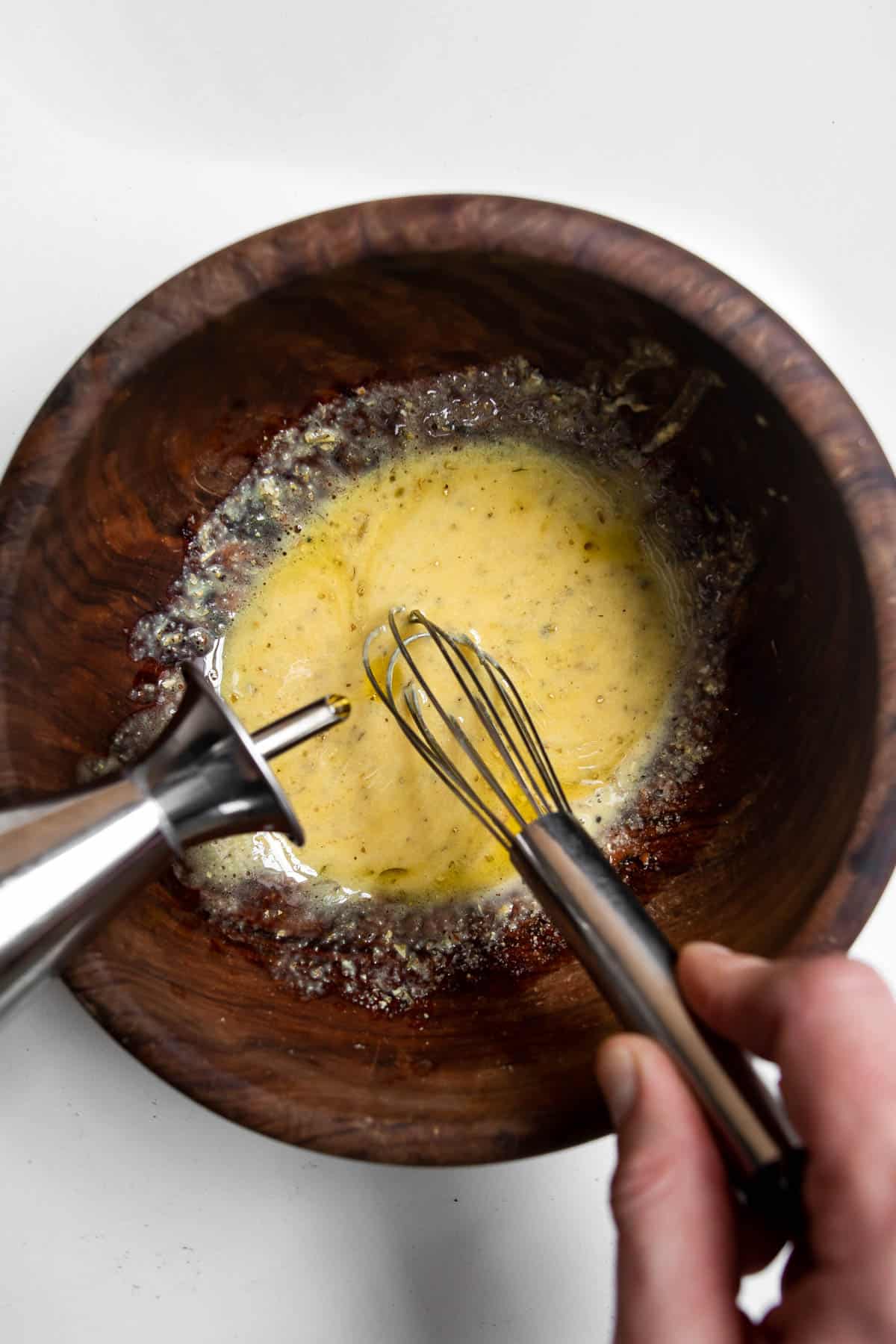 Hand whisking olive oil into dressing.