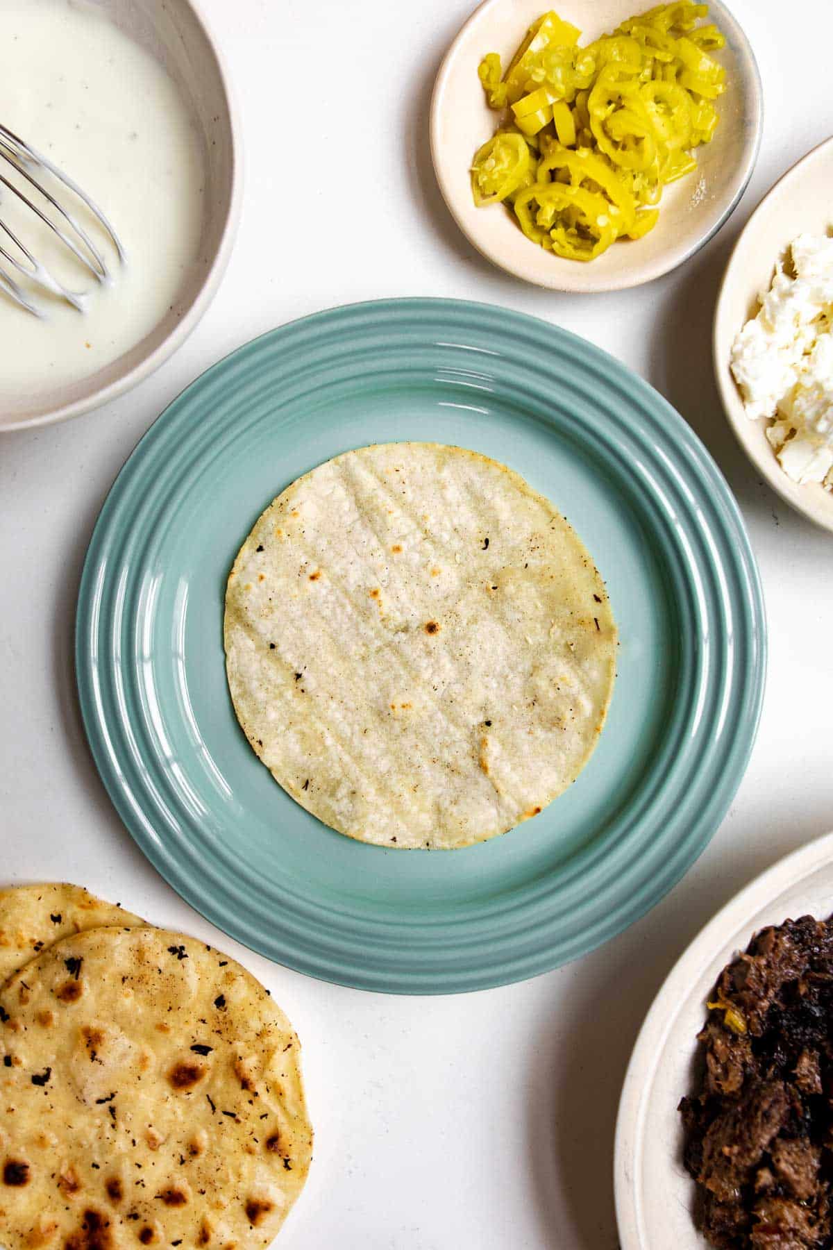 corn tortilla on a green plate with pepperoncini, sour cream, tortillas and meat around it.