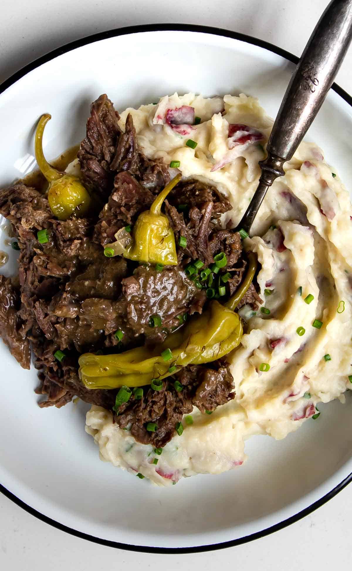 Mississippi pot roast with pepperoncini spooned over mashed potatoes with a spoon.