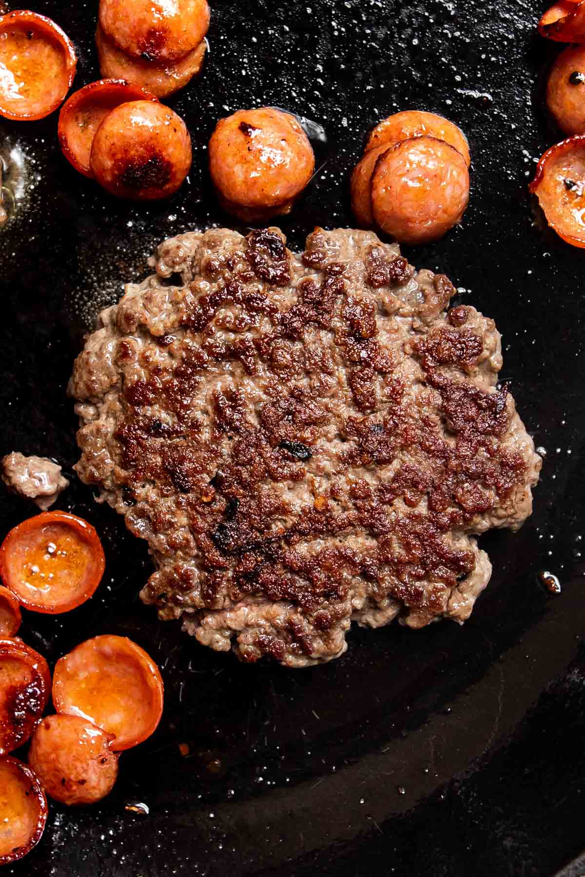 grilled burger and cooked pepperoni on a skillet.