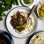 Mississippi pot roast with pepperoncini spooned over mashed potatoes with a spoon.