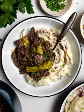 Mississippi pot roast with pepperoncini spooned over mashed potatoes with a spoon.