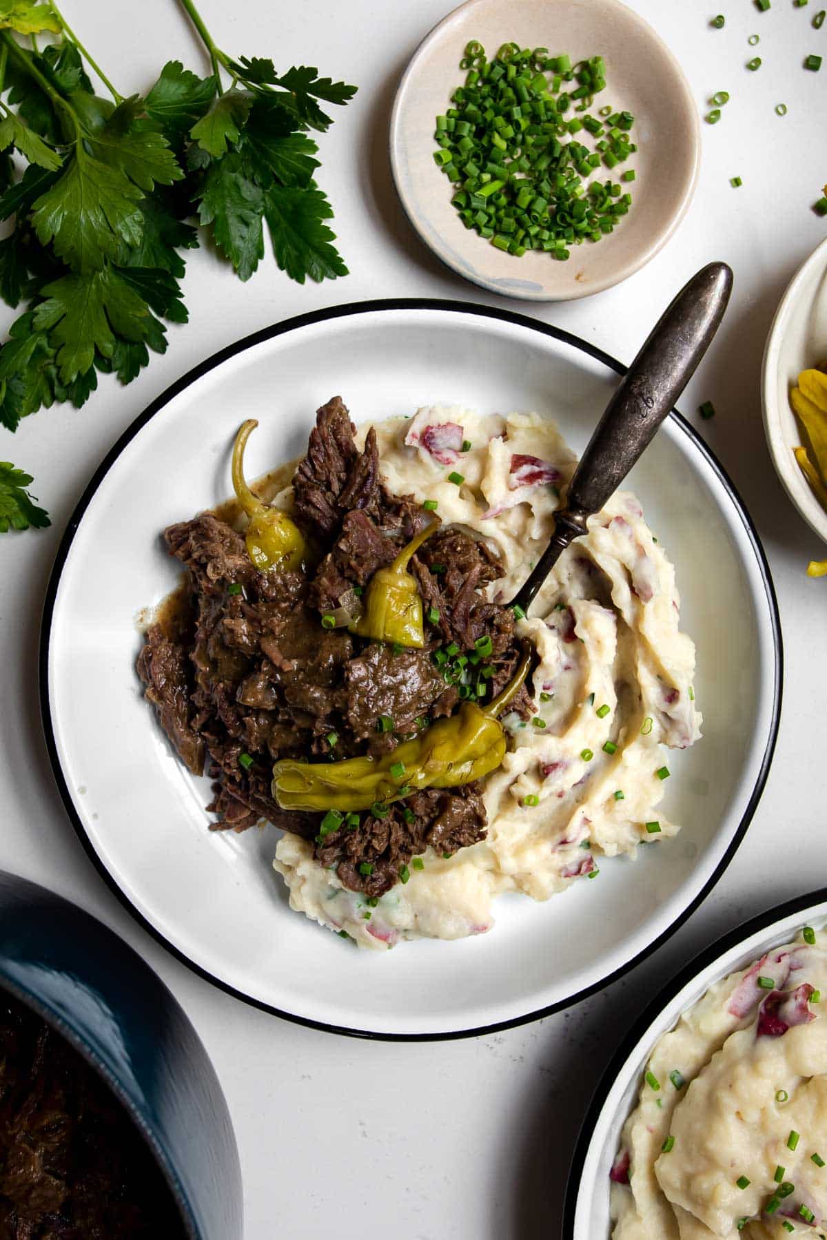 Mississippi pot roast with pepperoncini spooned over mashed potatoes with a spoon.