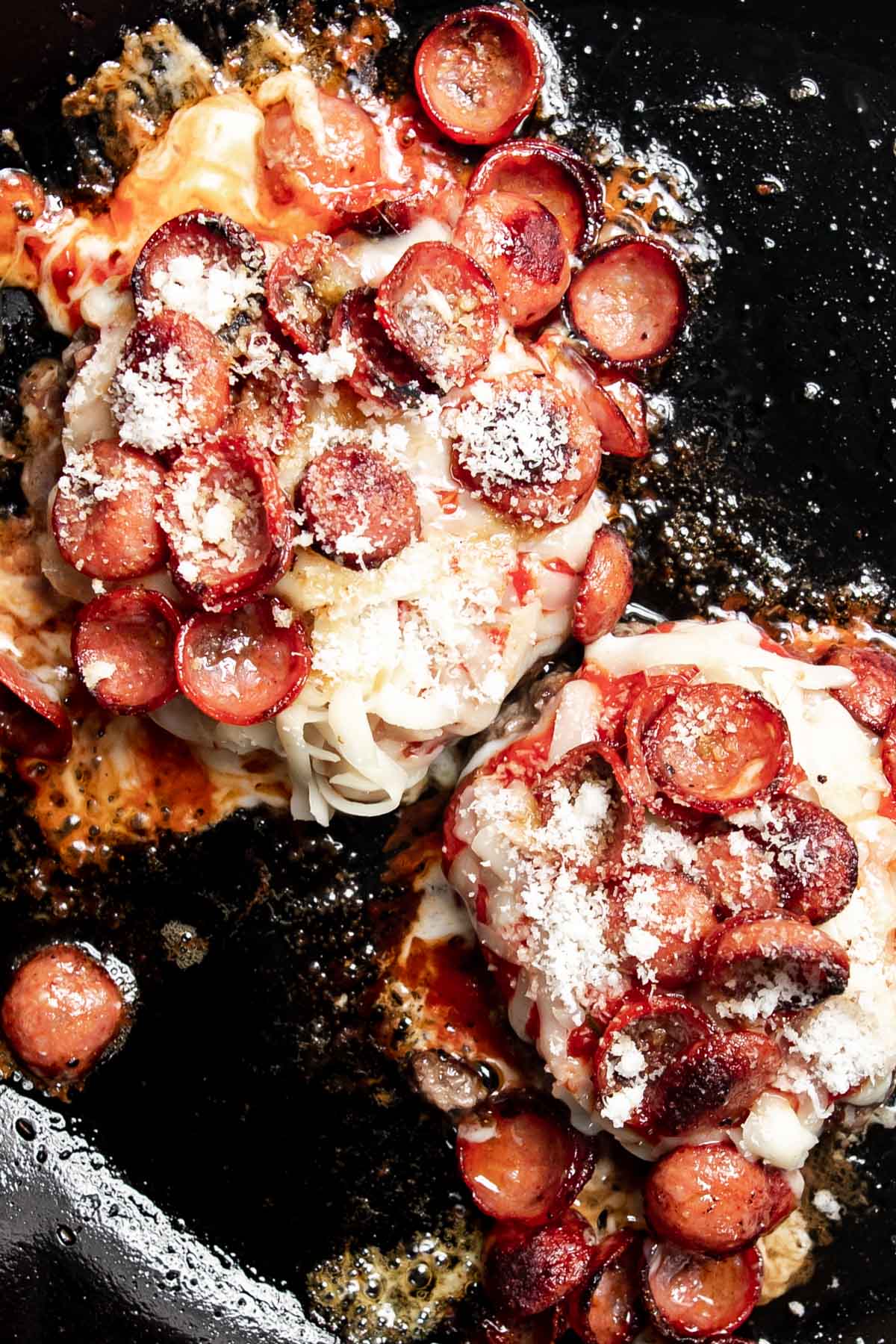 burger topped with melted mozzarella cheese, pepperoni and parmesan cheese in a skillet.
