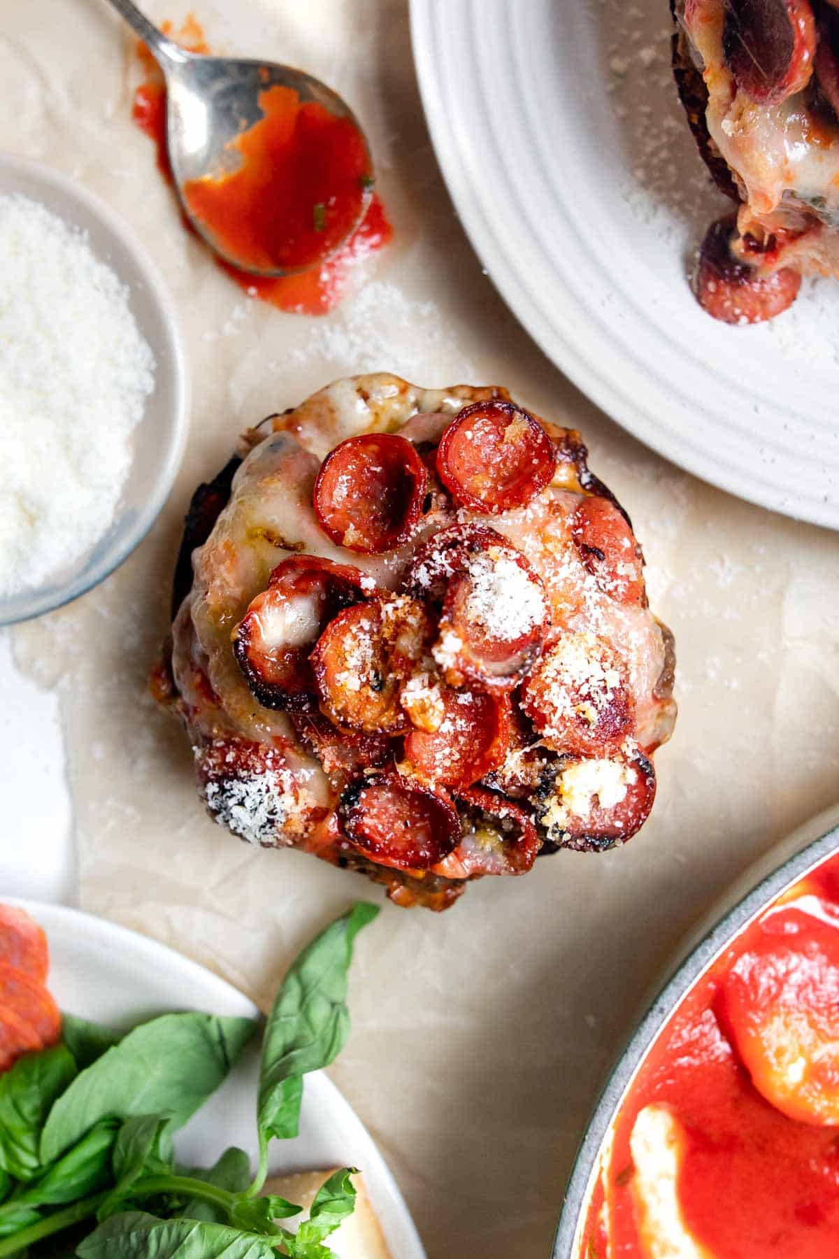 pizza burger on a bun with sauce, basil and parmesan cheese around it.