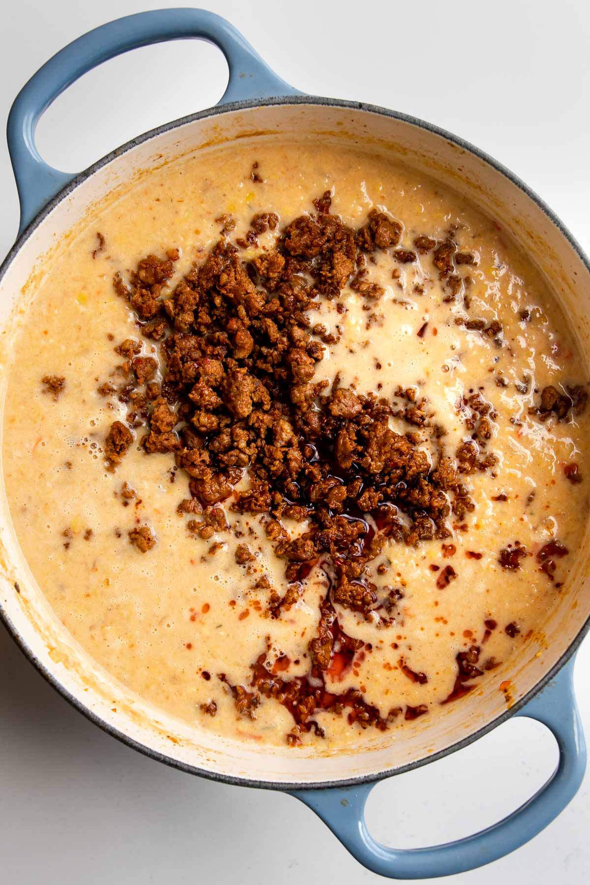 cooked sausage on top of blended corn chowder in a pot.