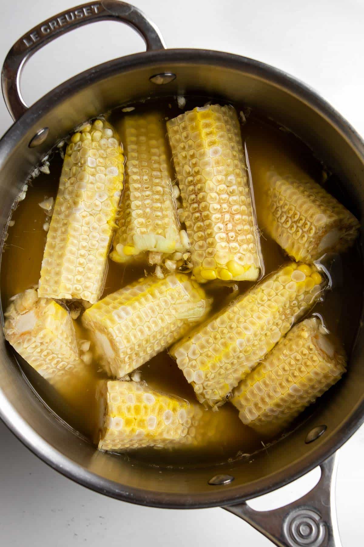 corn cobbs in a pot with chicken stock.