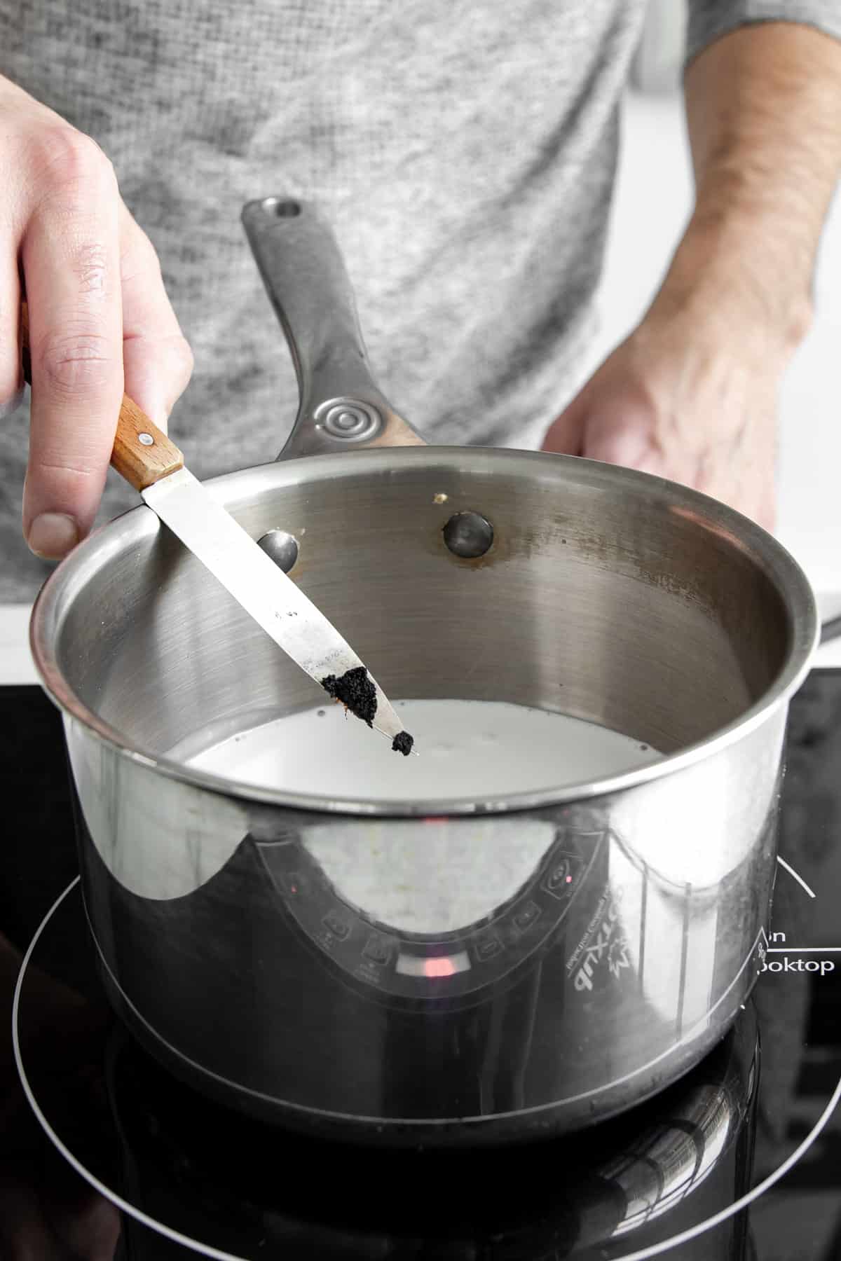 vanilla bean on a knife being added to coconut milk in a pot.