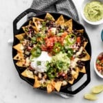 lentil nachos in a cast-iron skillet topped with sour cream, salsa, guacamole and jalapeño slices.