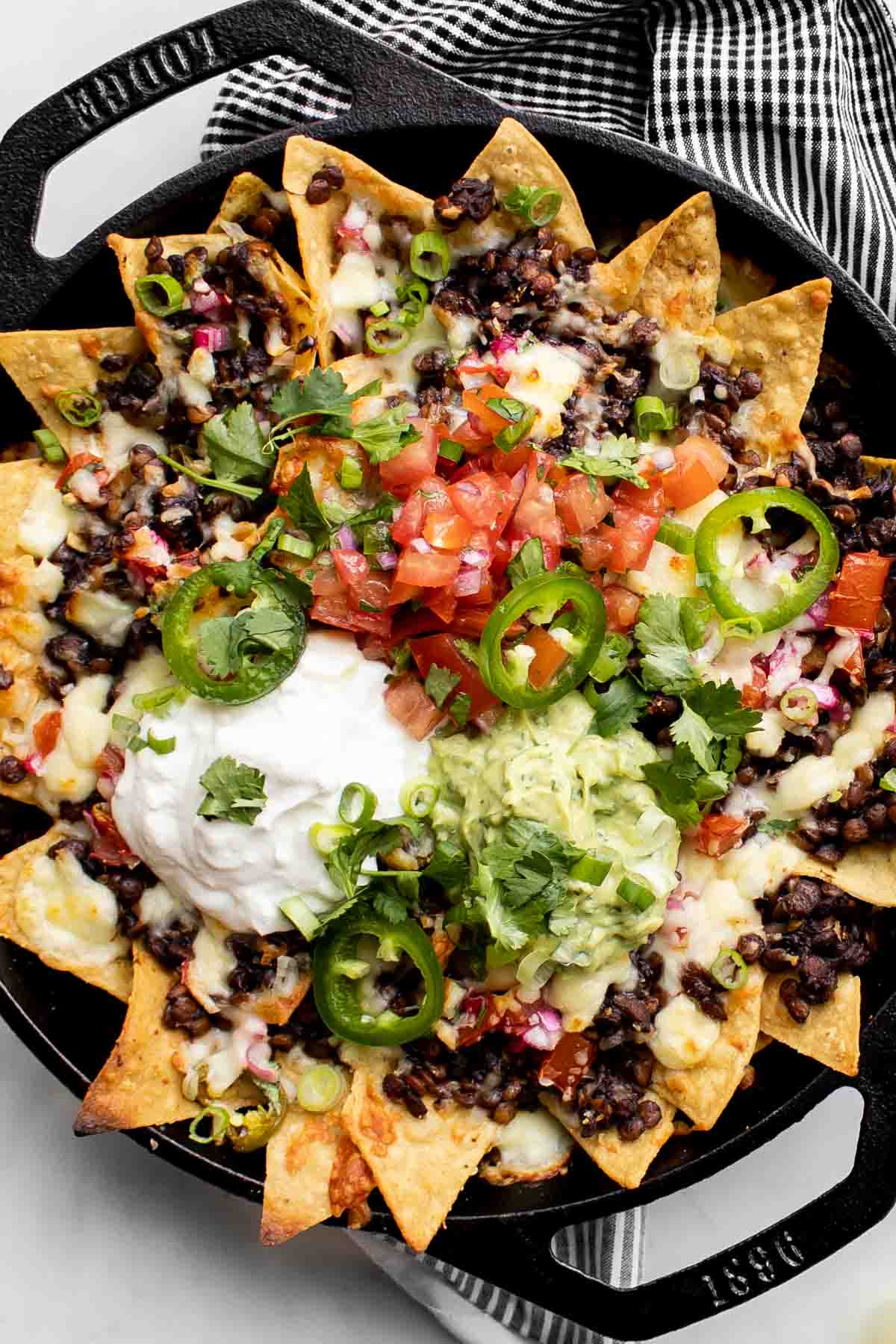 lentil nachos in a cast-iron skillet topped with sour cream, salsa, guacamole and jalapeño slices.