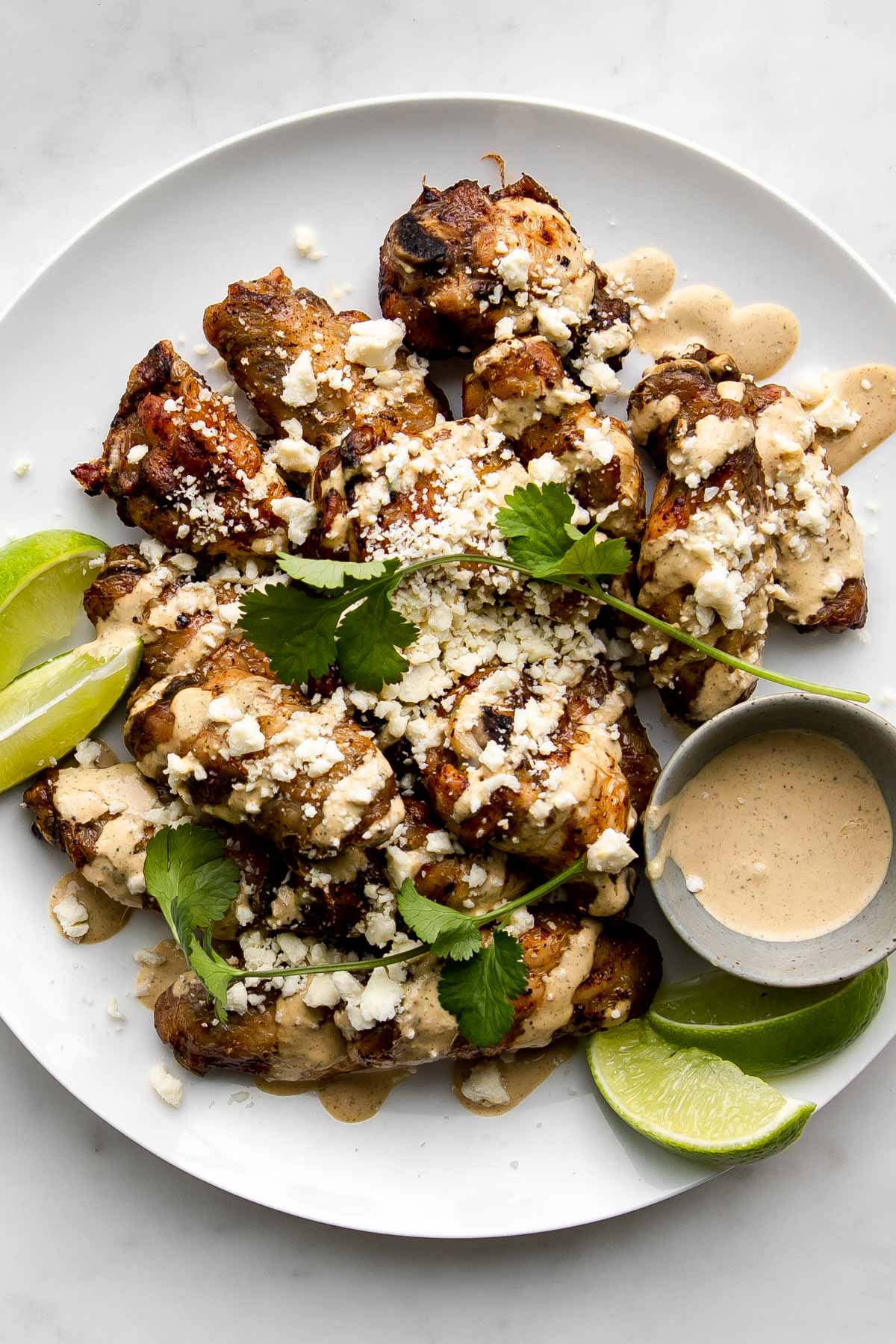 Mexican wings (elote wings) on a plate with limes and extra sauce in a bowl.