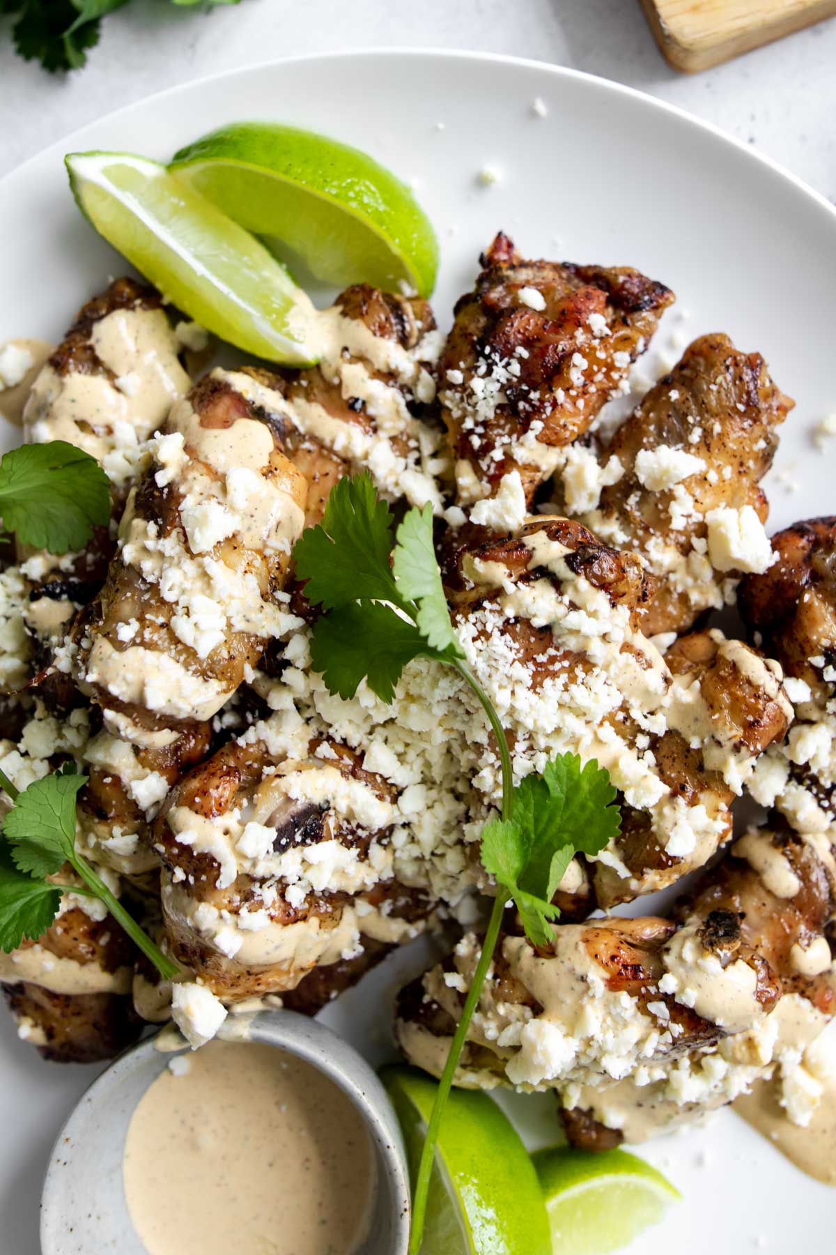 Mexican elote wings on a plate with limes and extra sauce in a bowl.