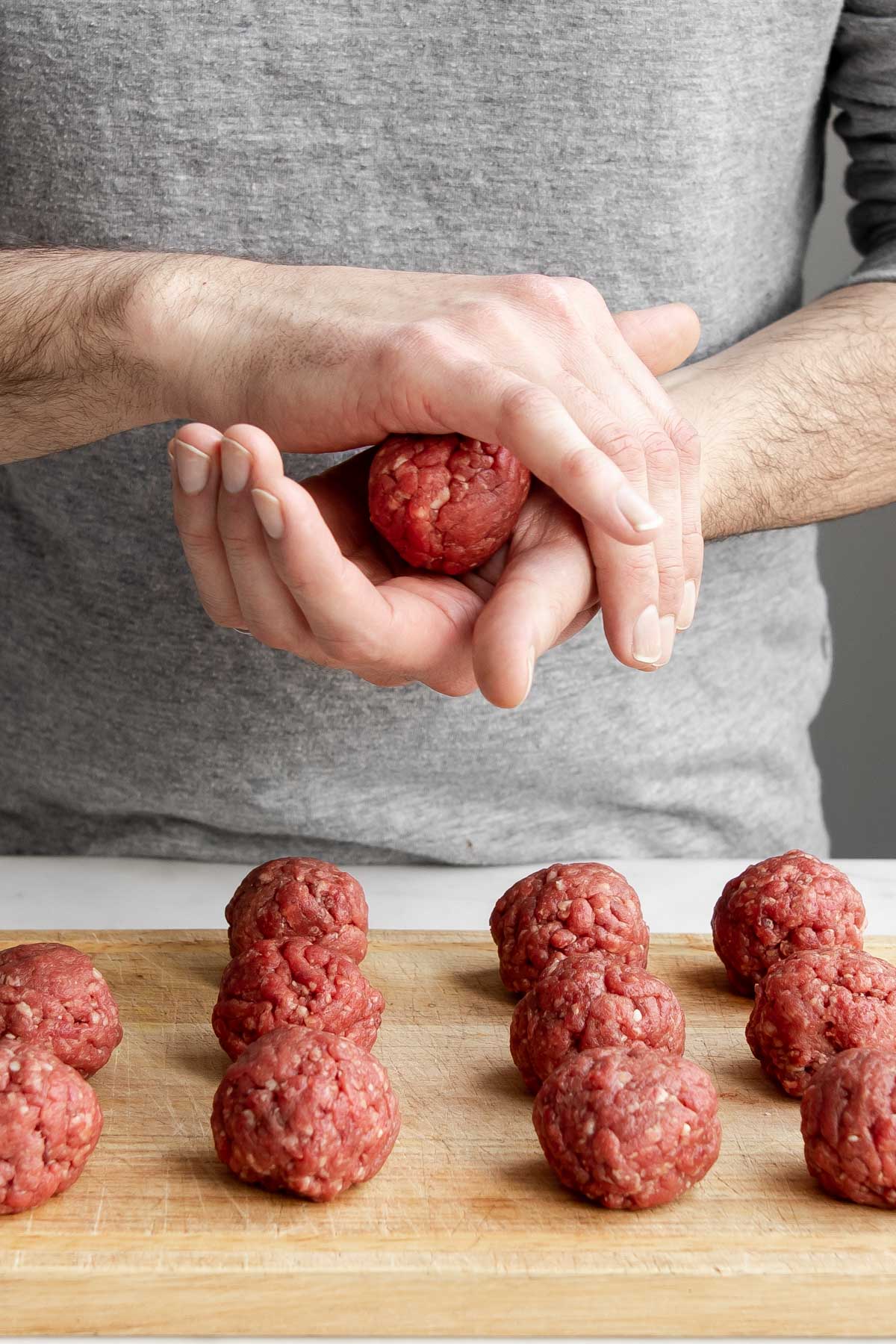 hand rolling beef meatball in hand with finished meatballs on a board below.