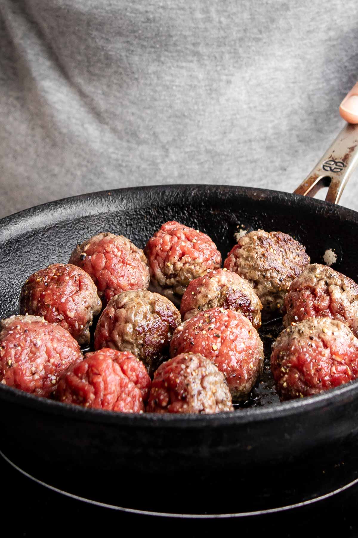 spicy meatballs cooking in a cast-iron pan.