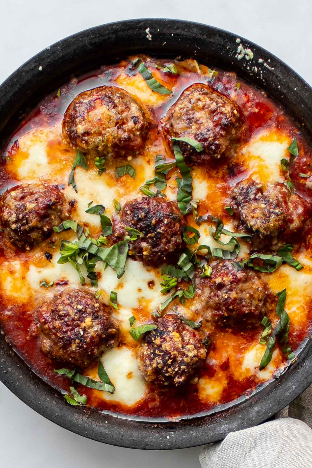 spicy meatballs with marinara sauce, baked mozzarella and fresh basil in a cast-iron skillet.