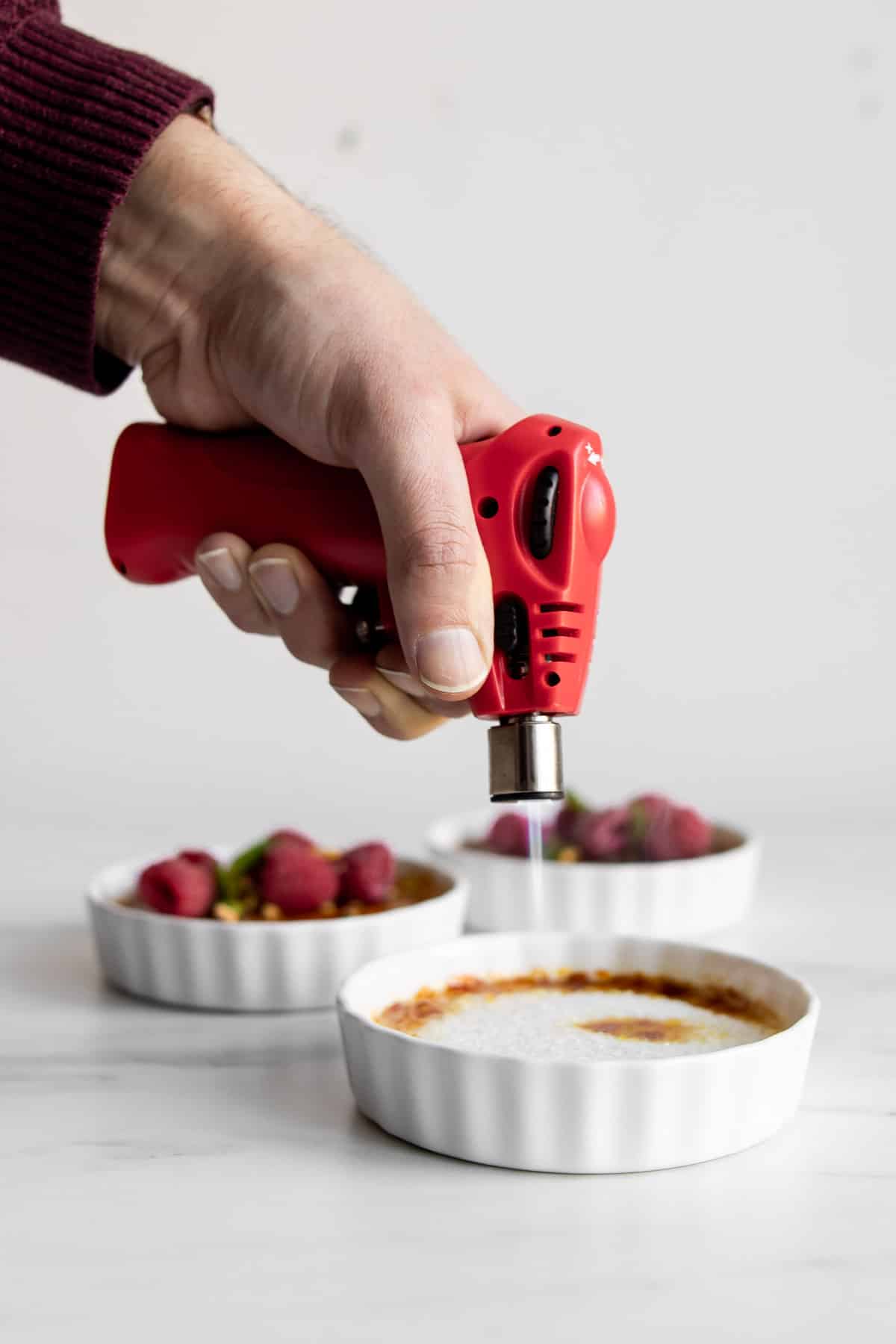 hand using a torch to caramelize the top of a coconut crème brûlée.
