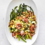 asparagus salad topped with boiled eggs, breadcrumbs, capers and prosciutto on a platter.